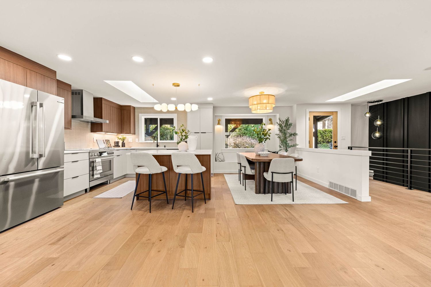 Modern open concept kitchen and dining area with light hardwood floors, white countertops and stainless steel appliances.