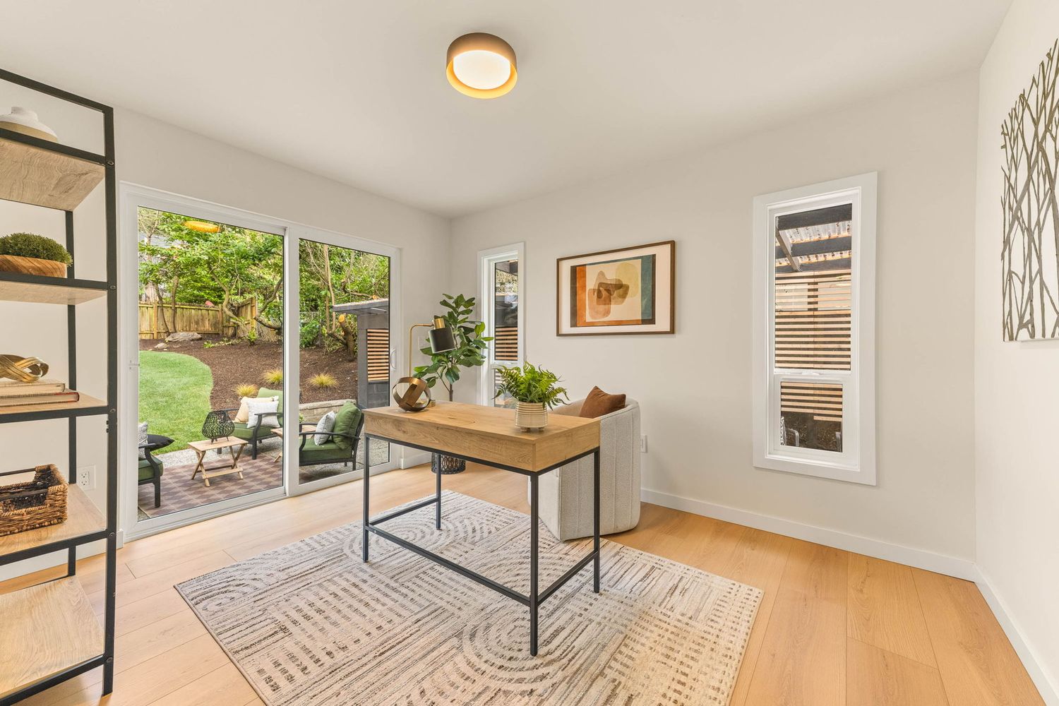 Modern open concept living room with hardwood floors, white walls, and large windows providing natural light.