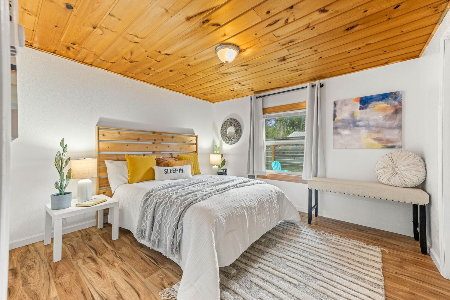 Cozy bedroom featuring knotty pine ceiling, white walls, and hardwood floors with natural light.