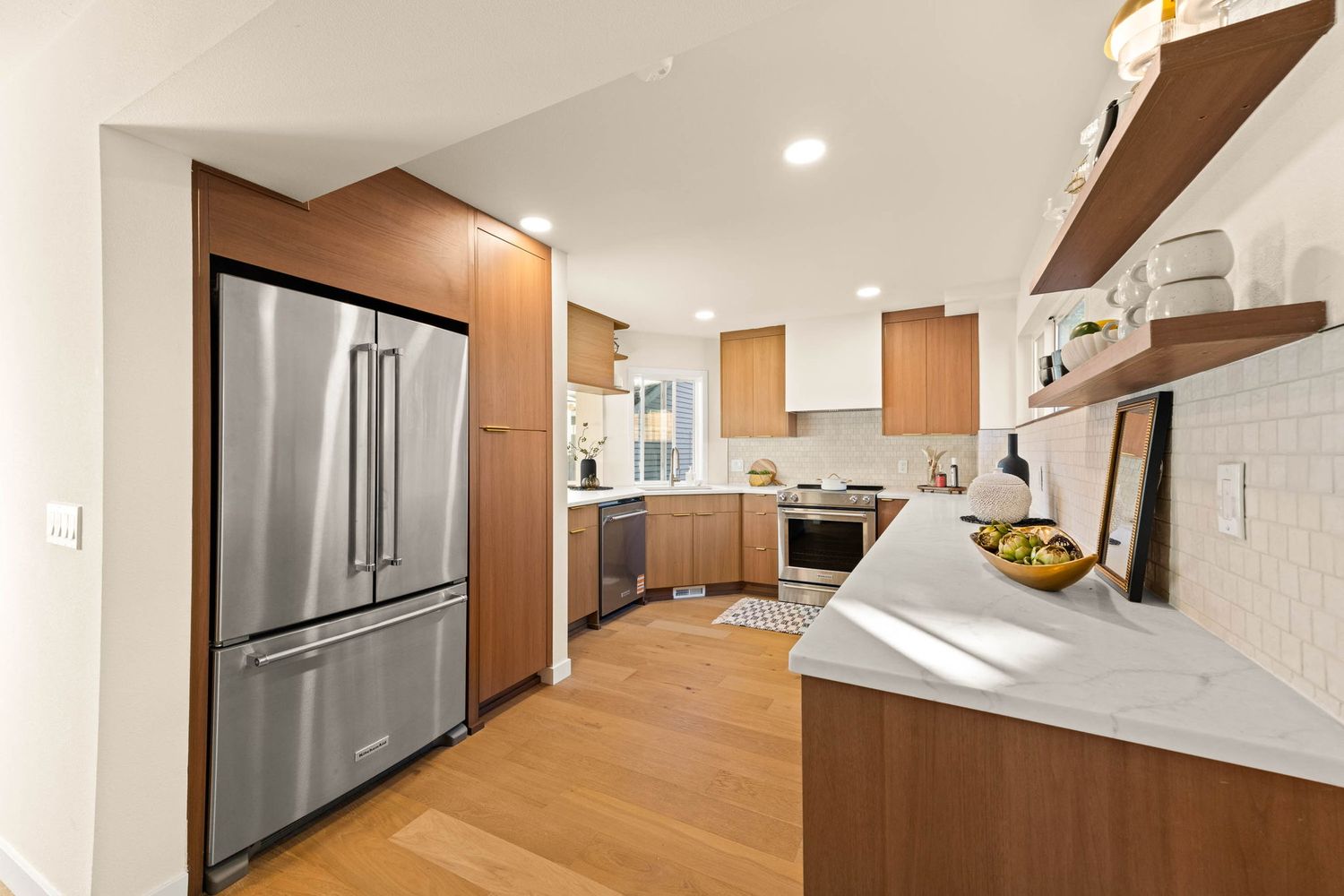 Modern kitchen and hallway interior with stainless steel appliances, white subway tile backsplash, and recessed lighting.