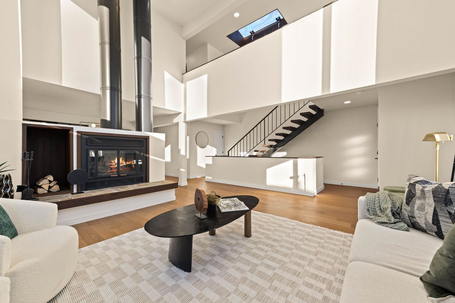 Modern open concept living room with white walls, hardwood floors, and black metal staircase railing.