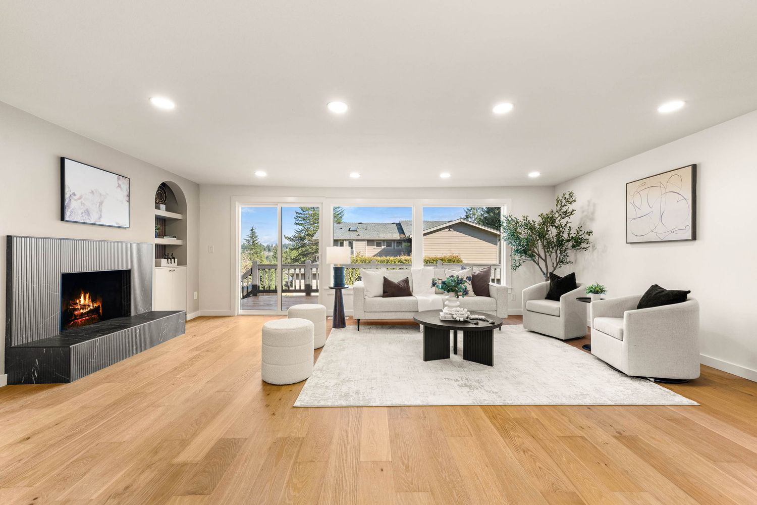 Modern living room with recessed lighting, hardwood floors, and a sleek fireplace along white walls.