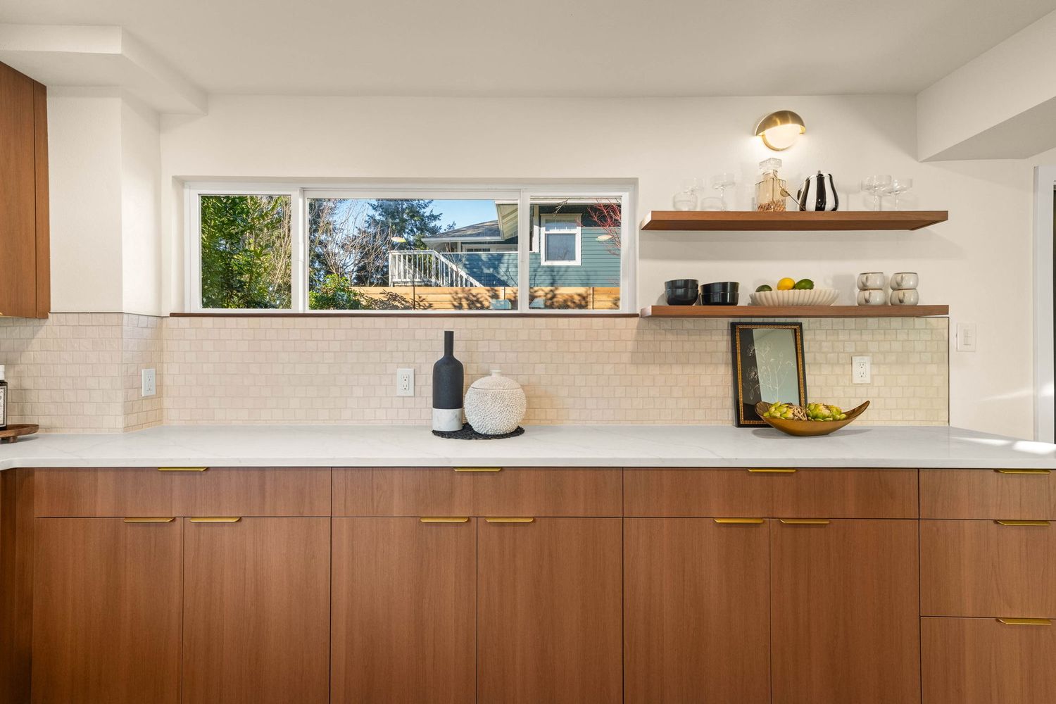 Minimalist kitchen interior with floating wood shelves and warm brown lower cabinets against white walls.