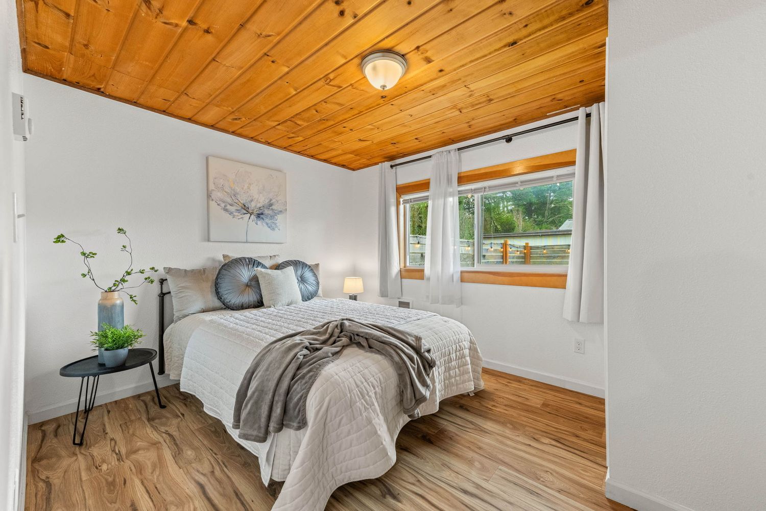 Bright bedroom with wood-paneled ceiling, hardwood floors, and large windows letting in natural light.