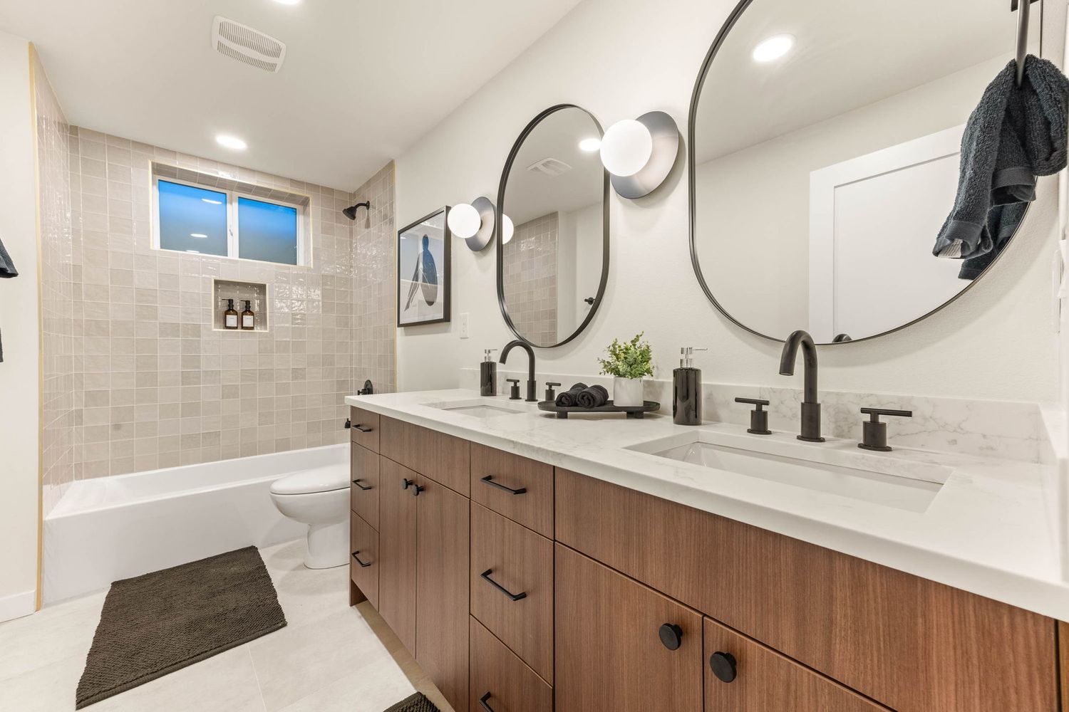 Contemporary bathroom with dual vanity, wood cabinets, white tile backsplash and round mirrors.