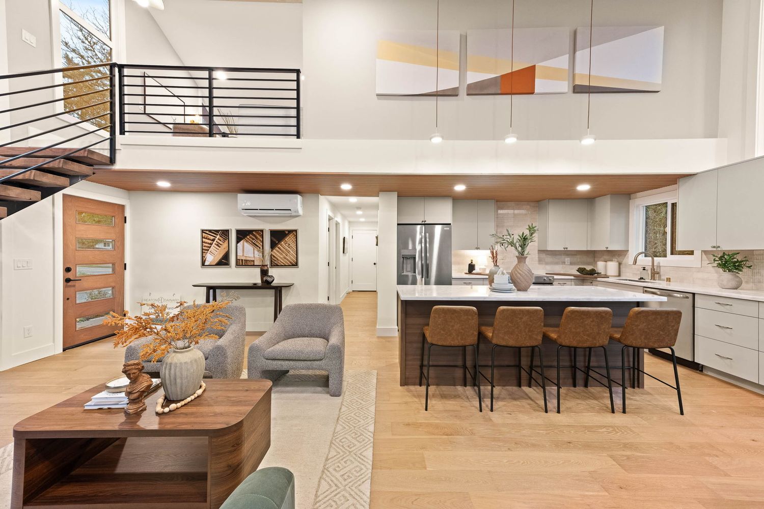 Modern open concept kitchen and living area with white cabinets, hardwood floors and recessed lighting.