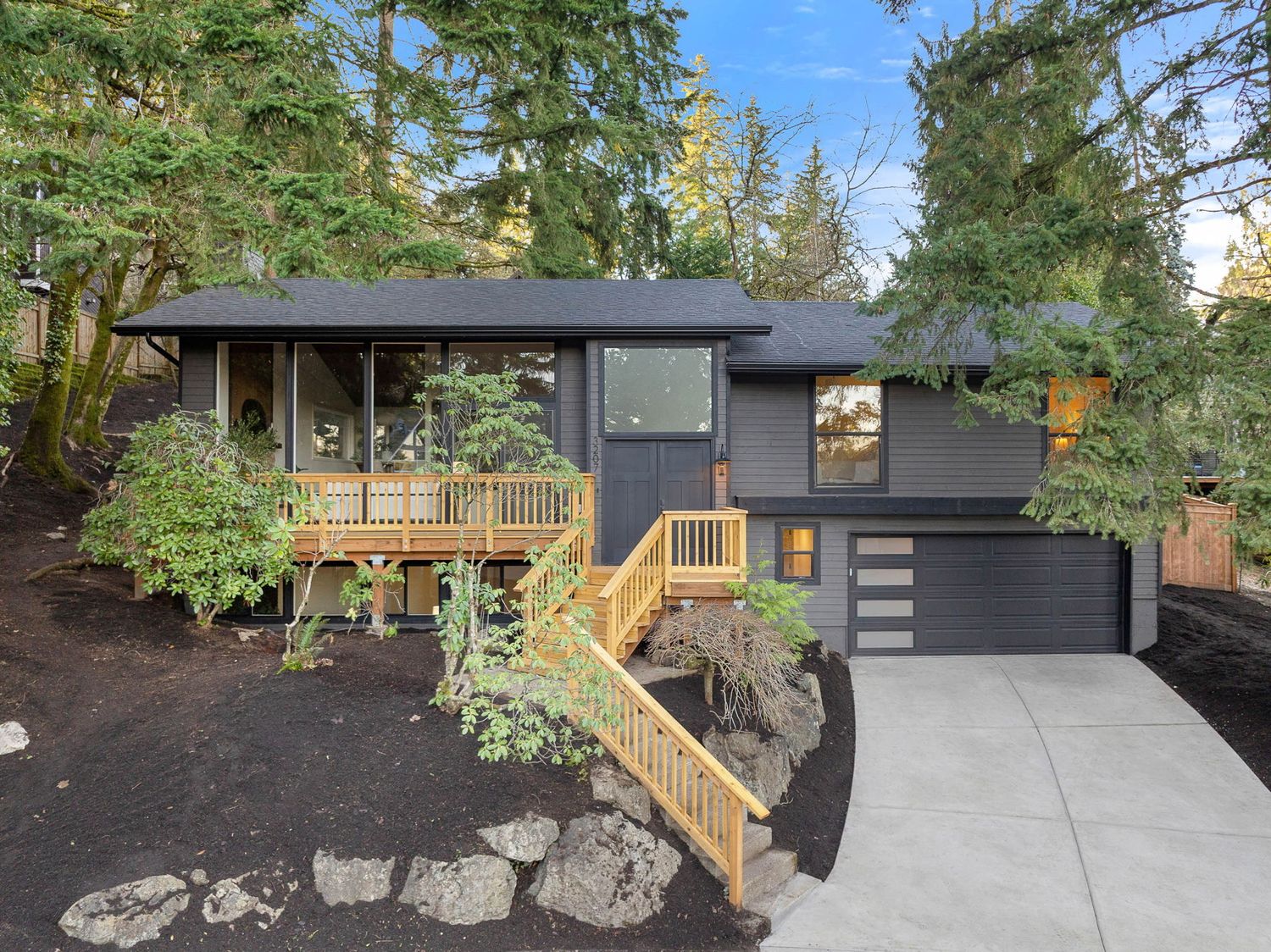 A panoramic view of a modern backyard featuring a concrete patio, wooden deck, and natural stone landscaping elements.