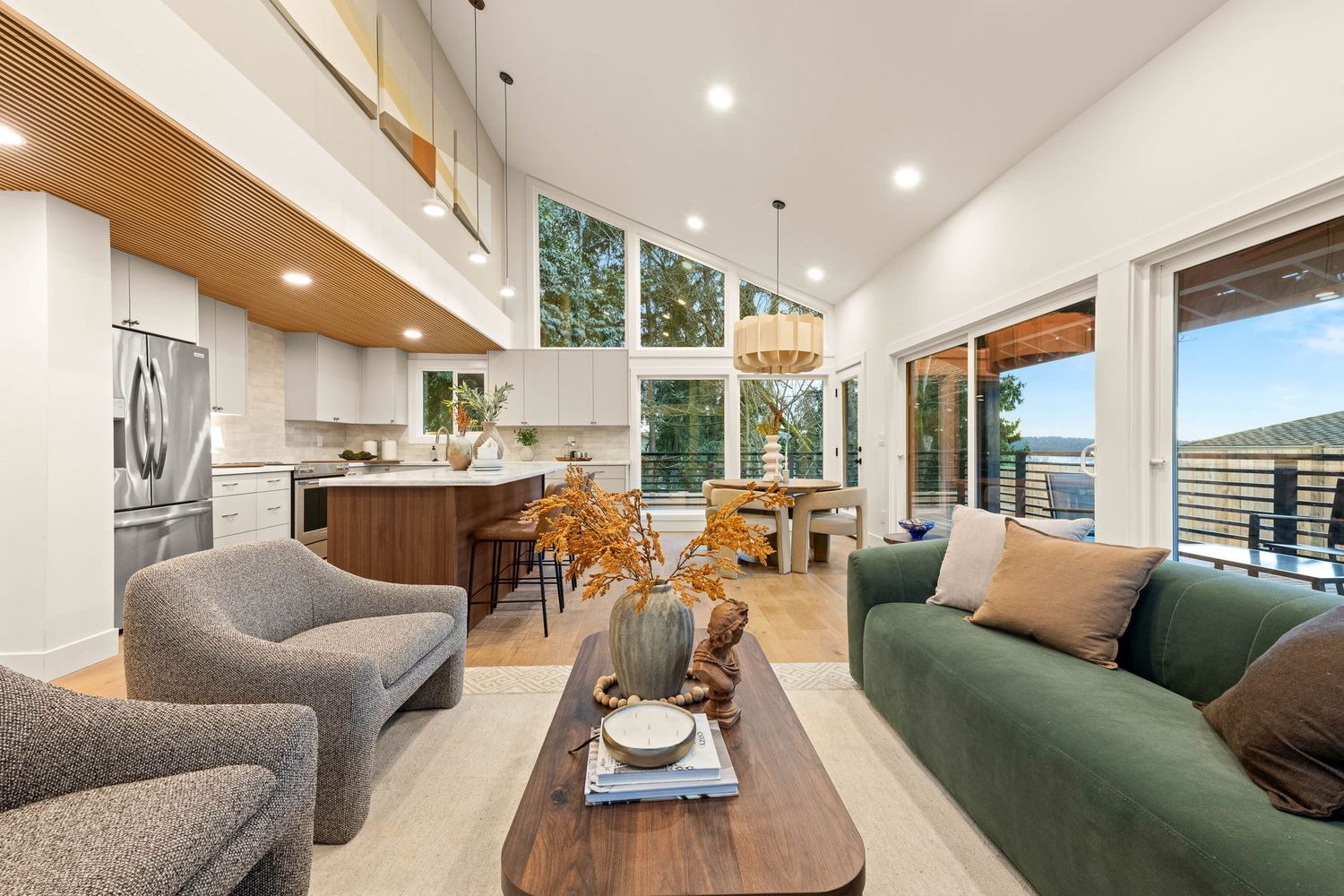 Modern open-concept living room with green accent chair, wood paneling, and recessed lighting showcases sleek design elements.