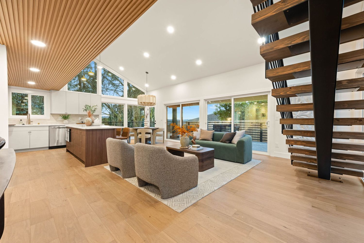 Modern living room features wood slat ceiling details, gray sectional sofa, and large windows overlooking outdoor greenery.