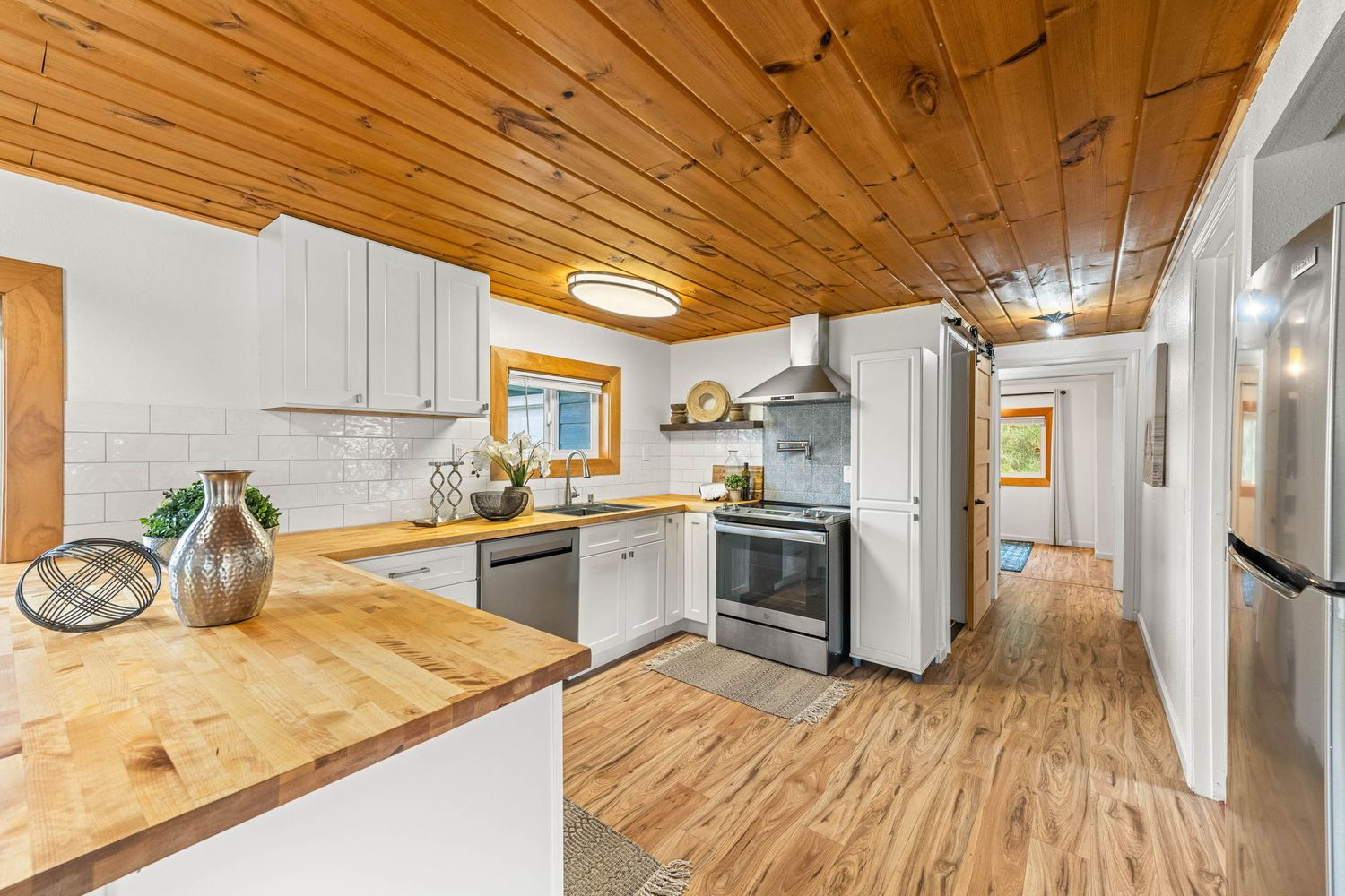Spacious open concept room with wood plank ceiling, white walls, and natural hardwood flooring throughout.