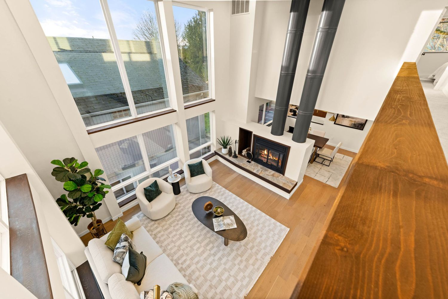 Two-story modern living space with floor-to-ceiling windows, floating fireplace, and geometric area rug on hardwood floors.
