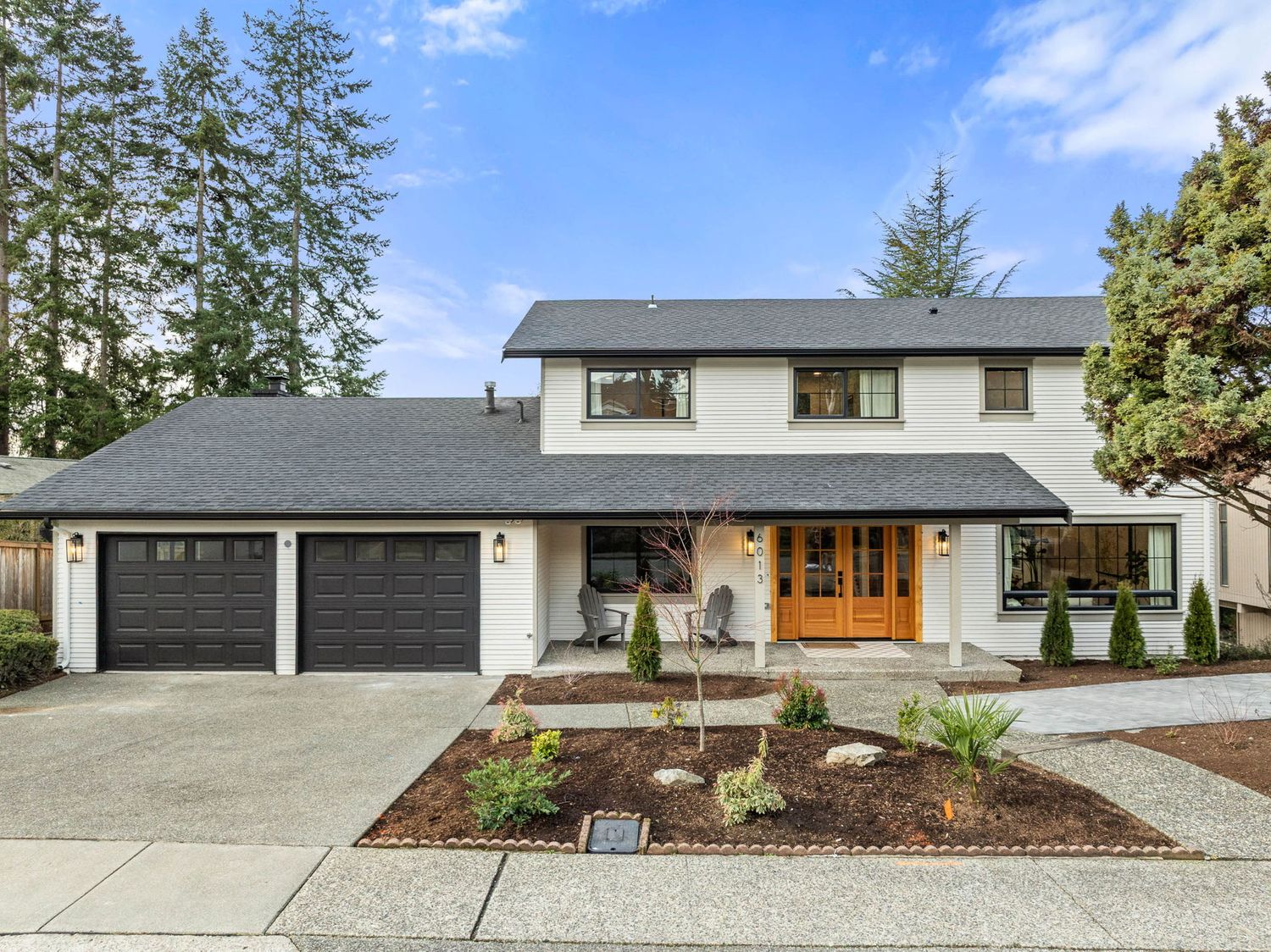 Modern two-story home with white exterior, wooden front door, and three-car garage featuring fresh landscaping and mulch beds.