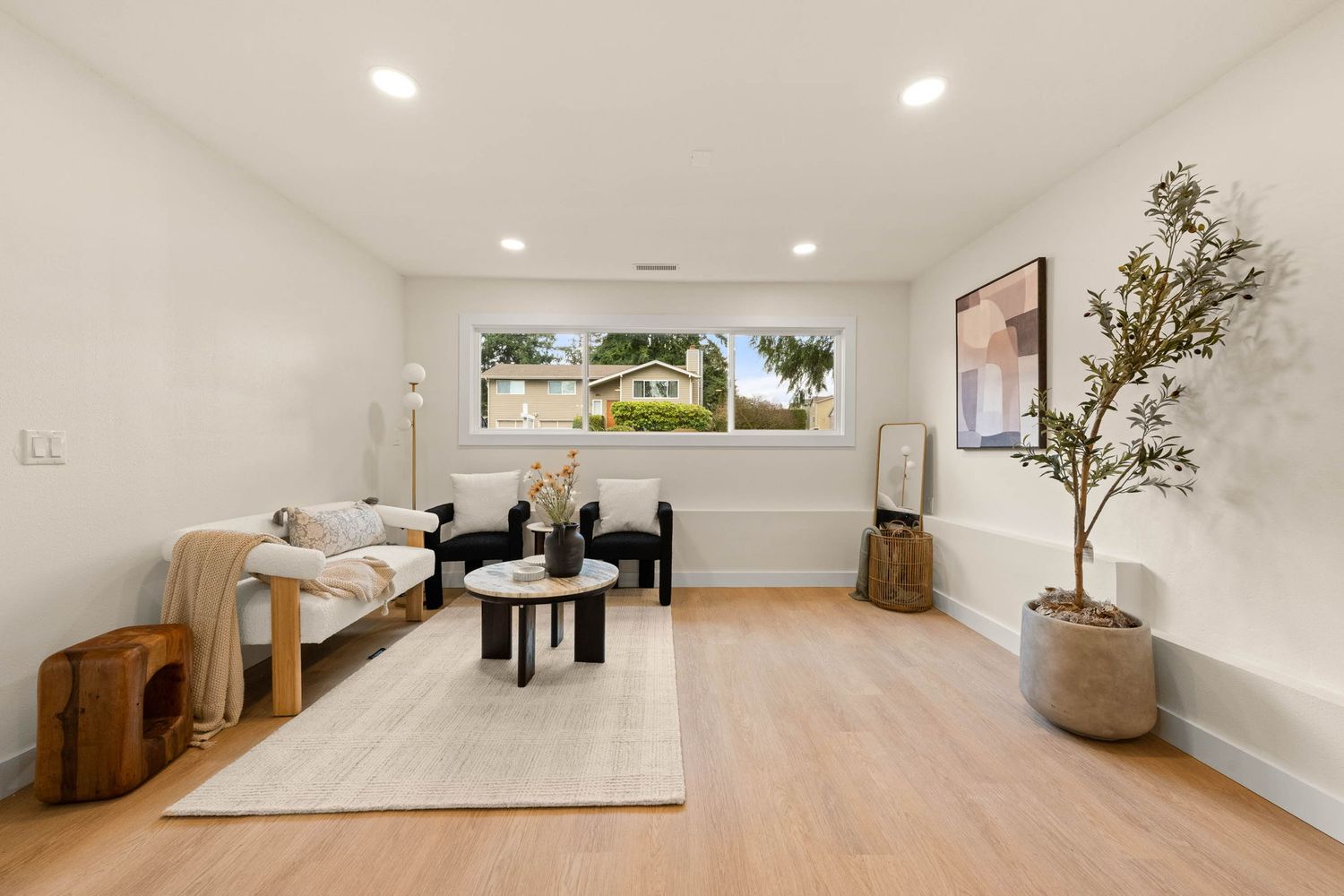 Modern open concept living room with white walls, recessed lighting, and hardwood flooring showcases minimalist design.