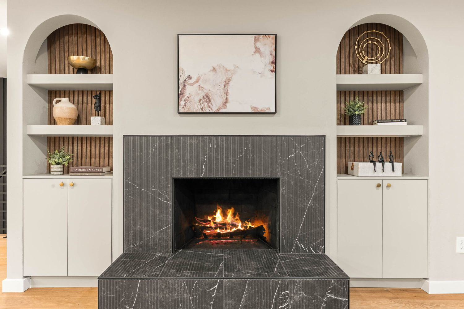 Contemporary living room with built-in arched shelving, marble fireplace, and minimalist white and grey decor.