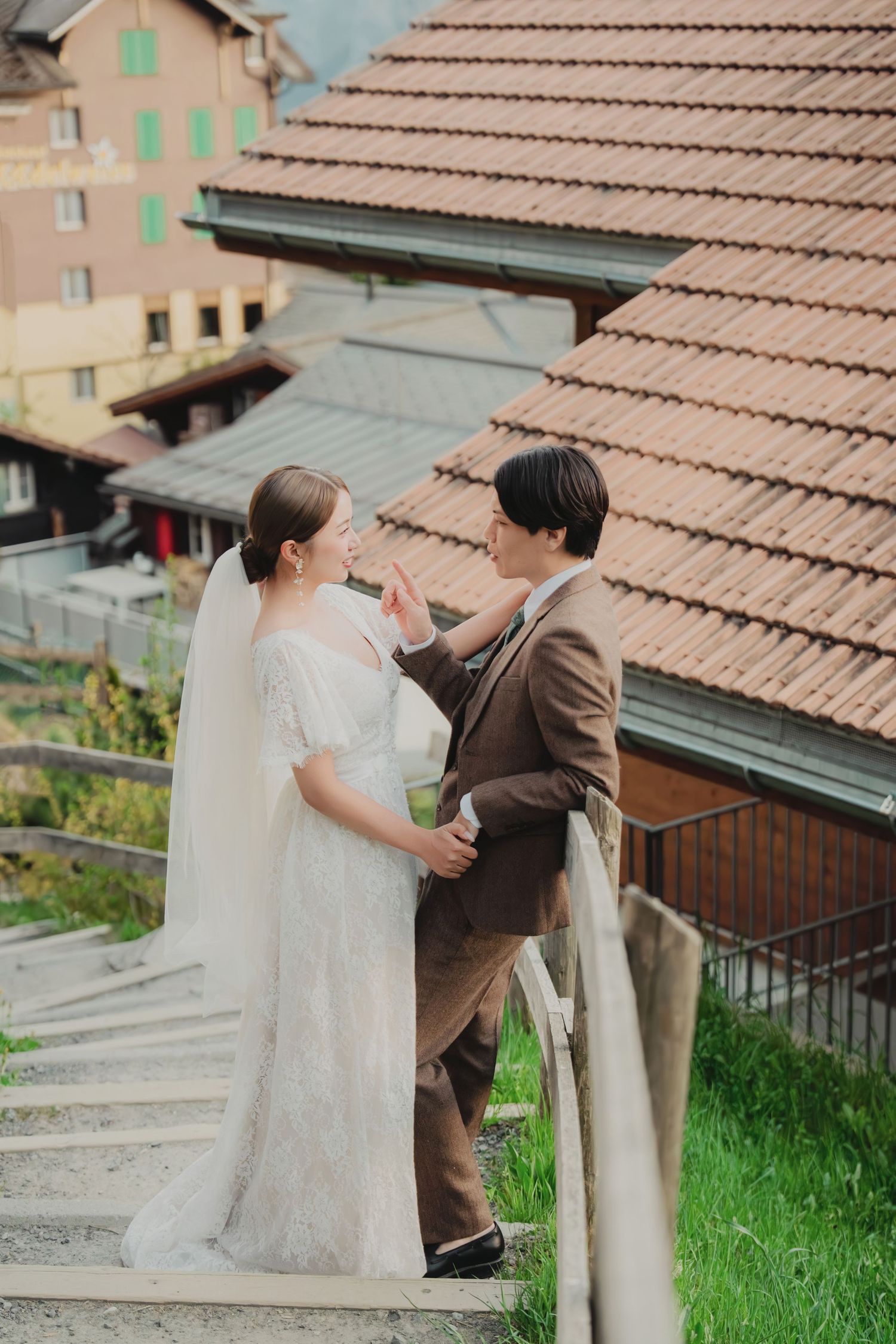 Bride and groom sharing a tender moment on stone steps beside traditional Swiss chalet buildings.
