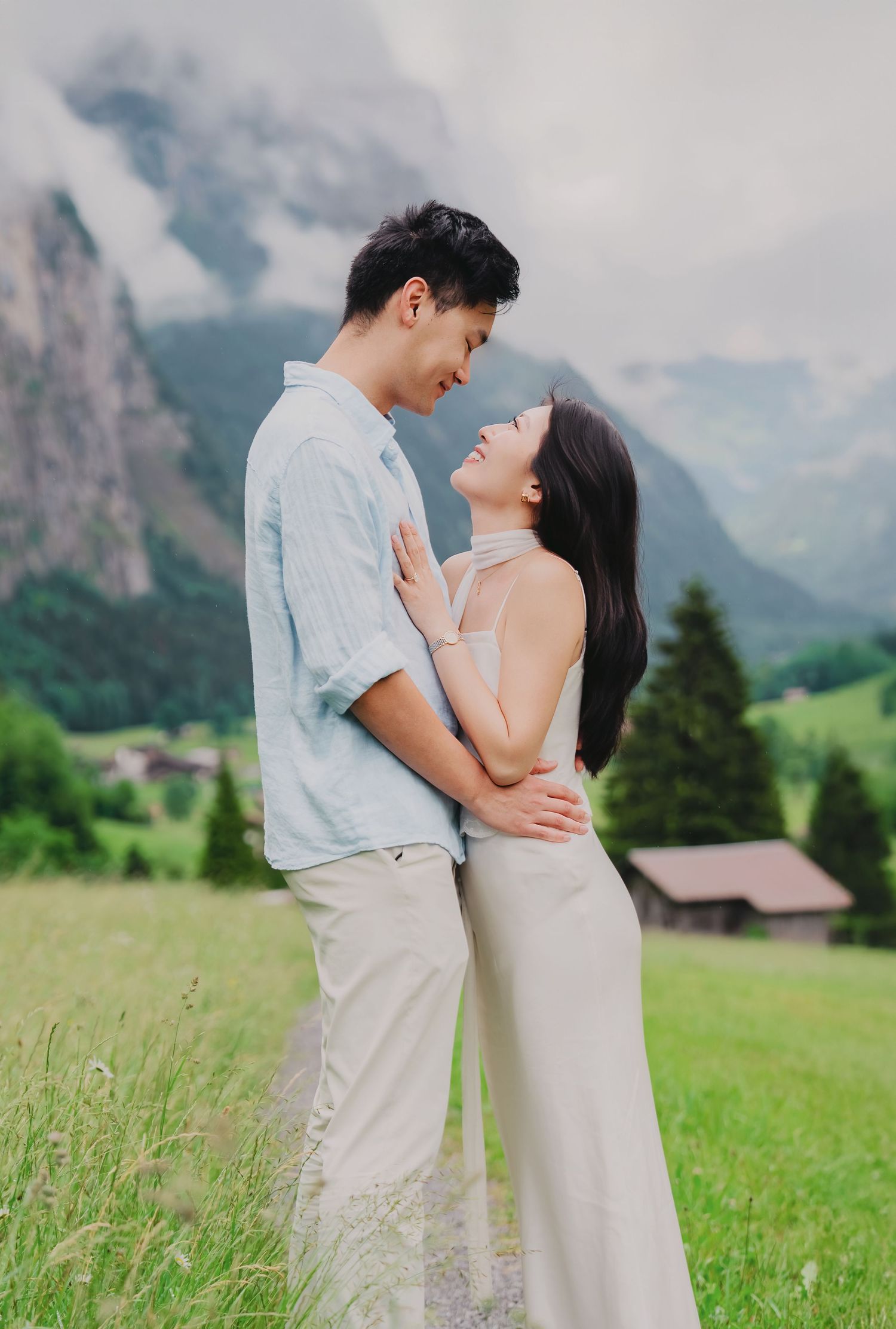 Couple gazes lovingly at each other while embracing in a lush green Swiss alpine meadow with mountains behind.