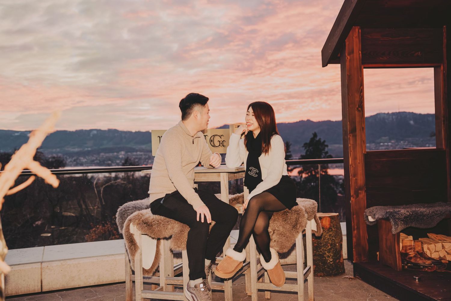 Romantic couple seated on white chairs on a mountain deck during a beautiful pink sunset.