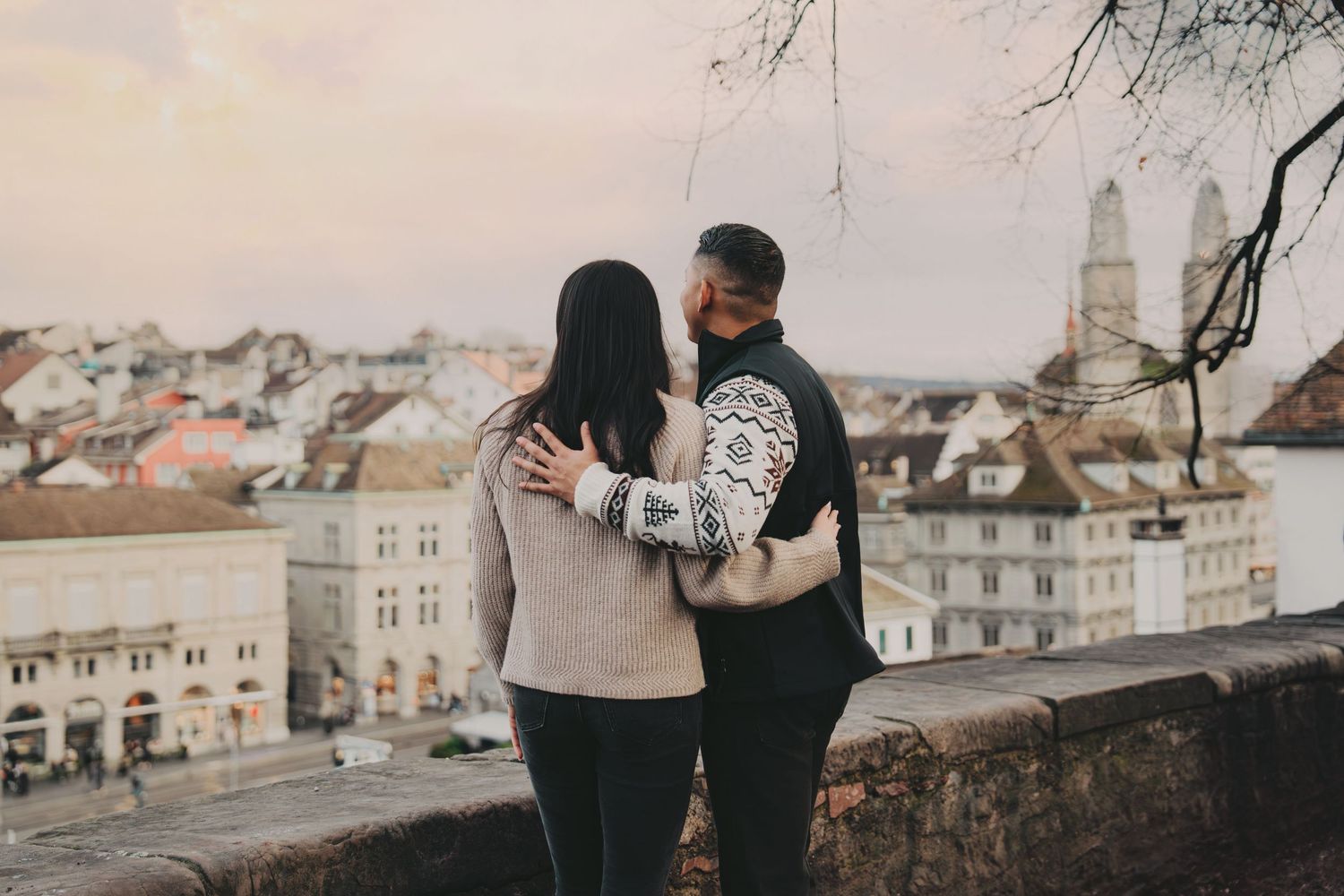 Couple embracing while overlooking a beautiful European city skyline at dusk.