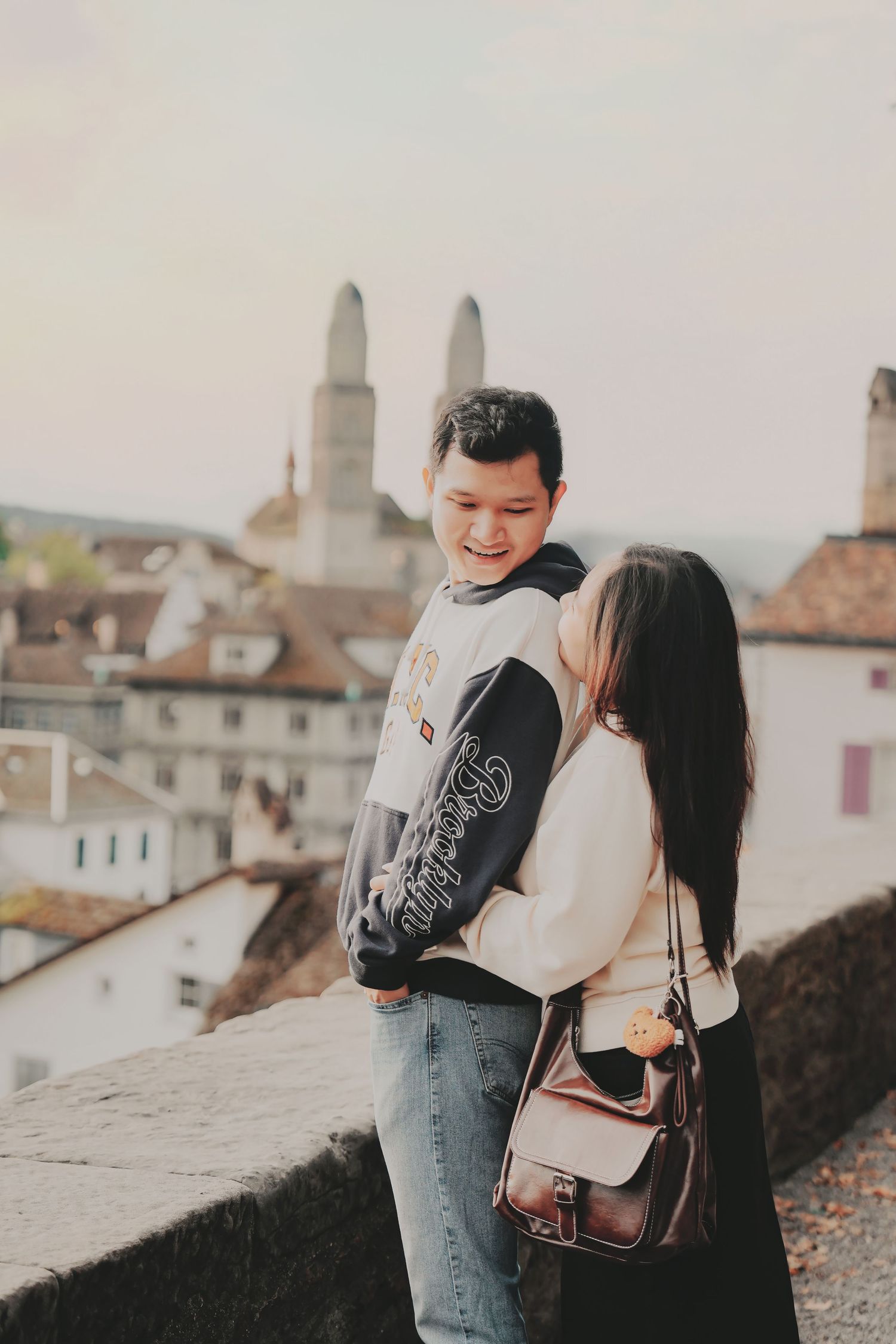 Laughing Asian couple embracing on a terrace overlooking the rooftops of Zurich old town.