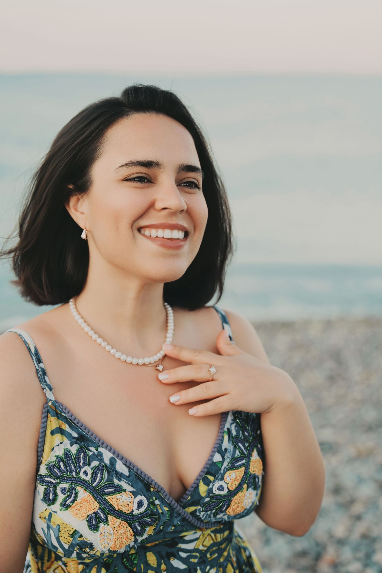Smiling brunette woman wearing floral dress and pearl necklace at pebble beach.