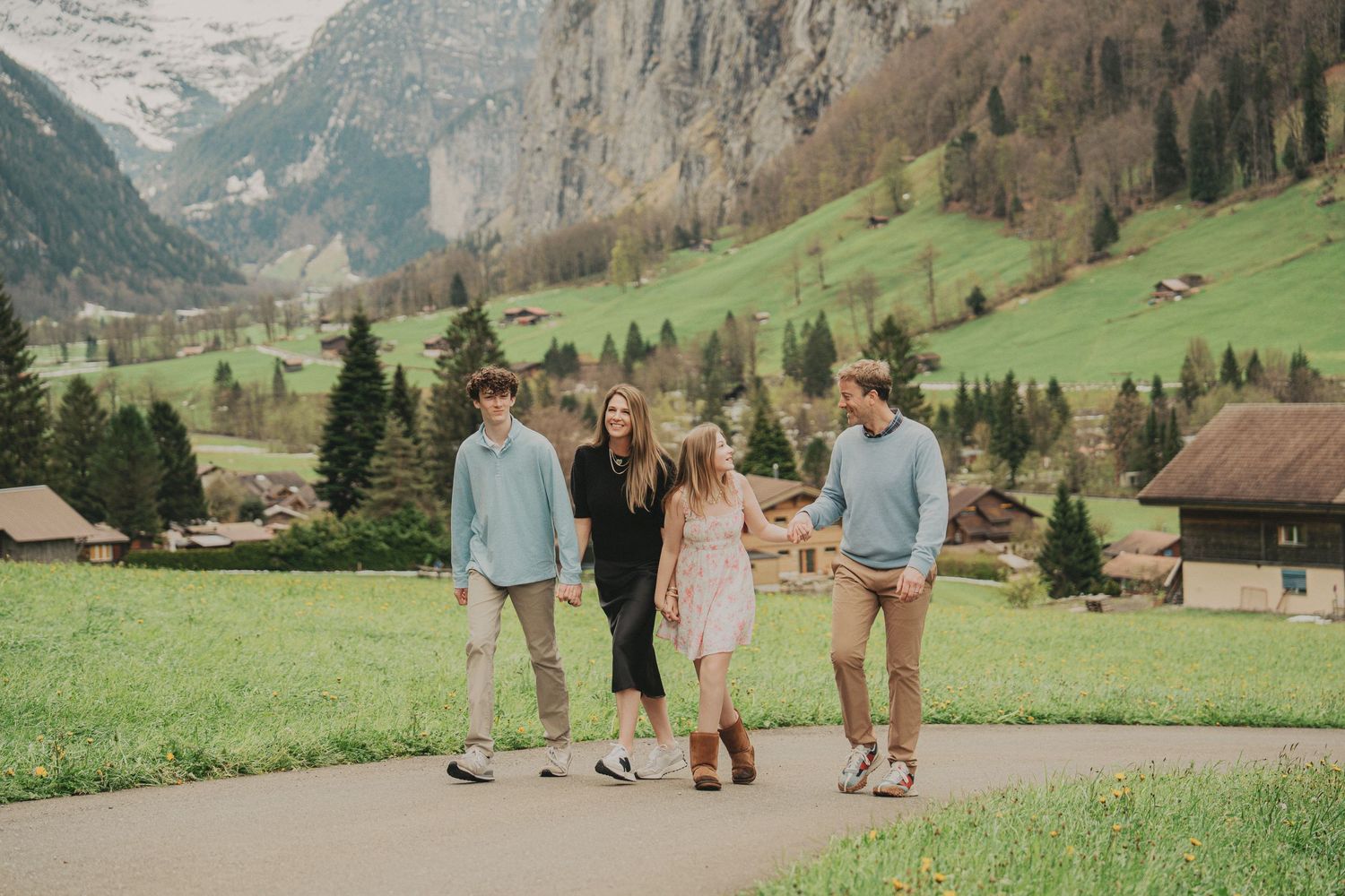Family of four laughing and walking together on a scenic path in the Swiss Alps village.