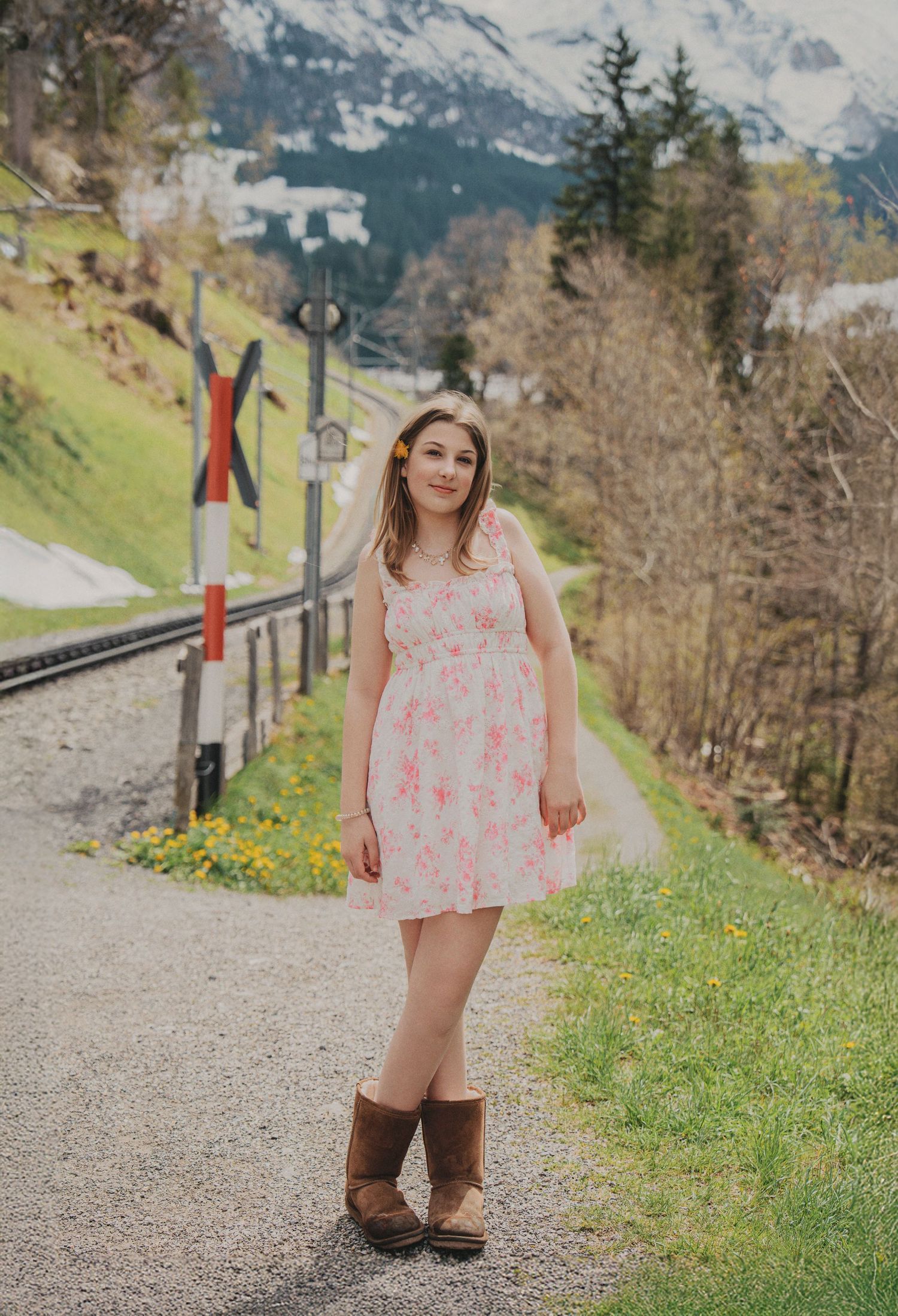 Young girl in pink floral dress and brown boots standing on a mountain road in Switzerland.