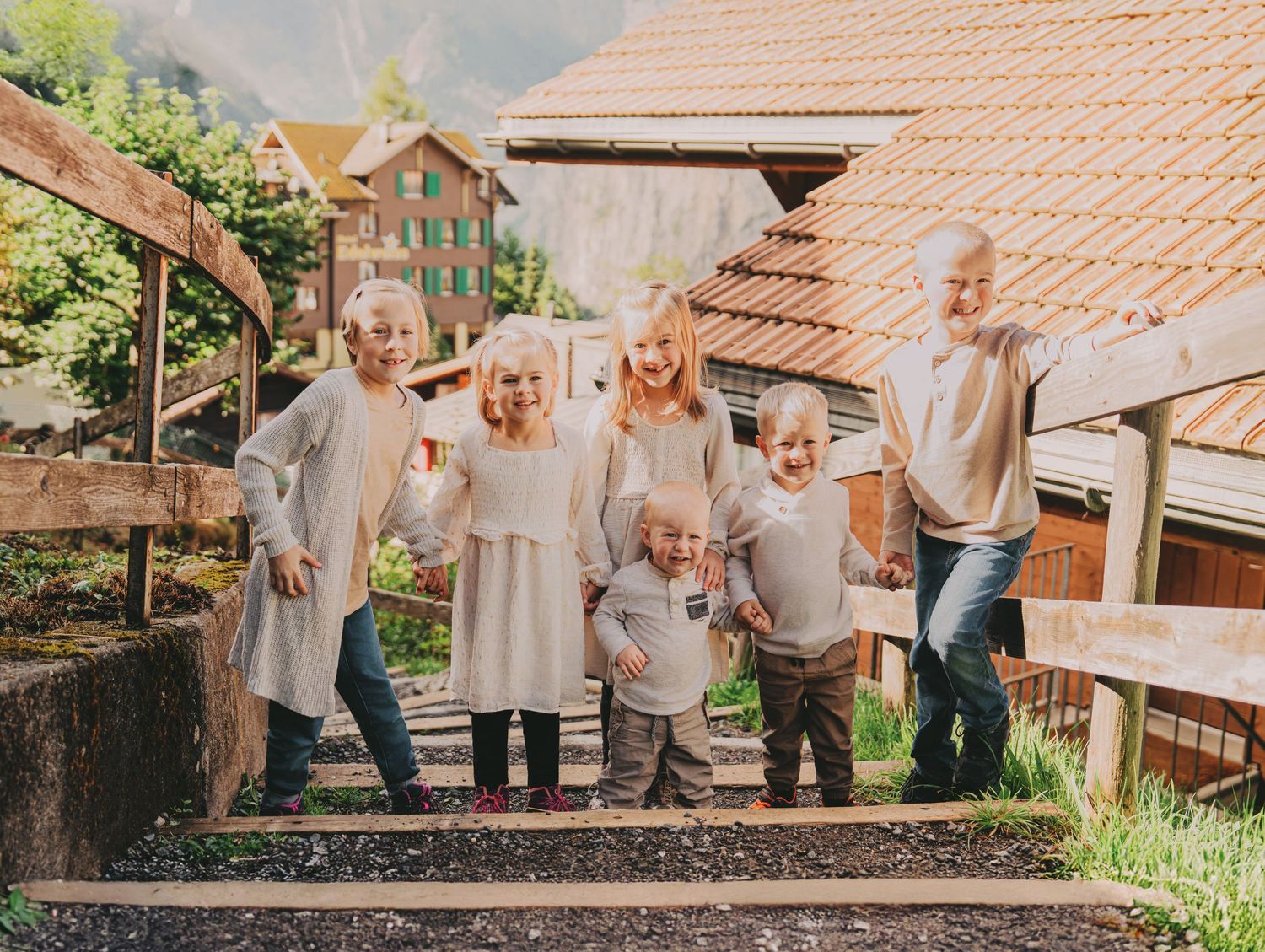 Group of seven blonde children posing on stone steps in a Swiss Alpine village.