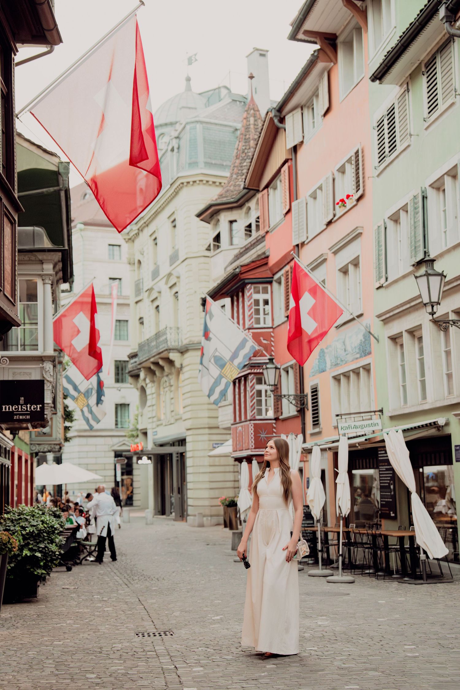 Woman in cream dress walks cobblestone street lined with Swiss flags in old town Zurich, Switzerland.