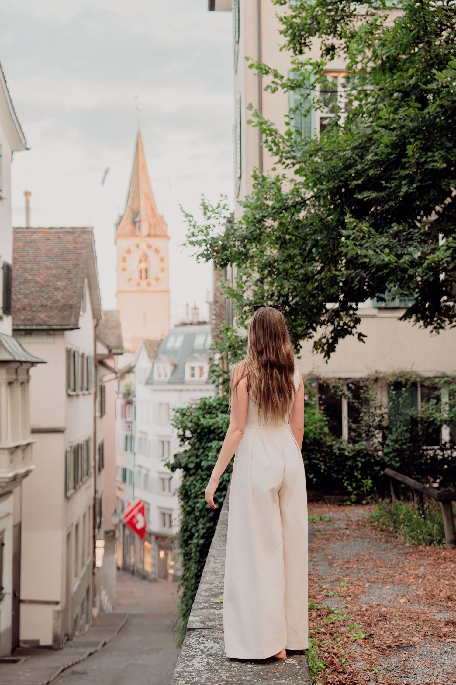 Woman in cream dress viewed from behind overlooking Zurich old town with church tower visible.