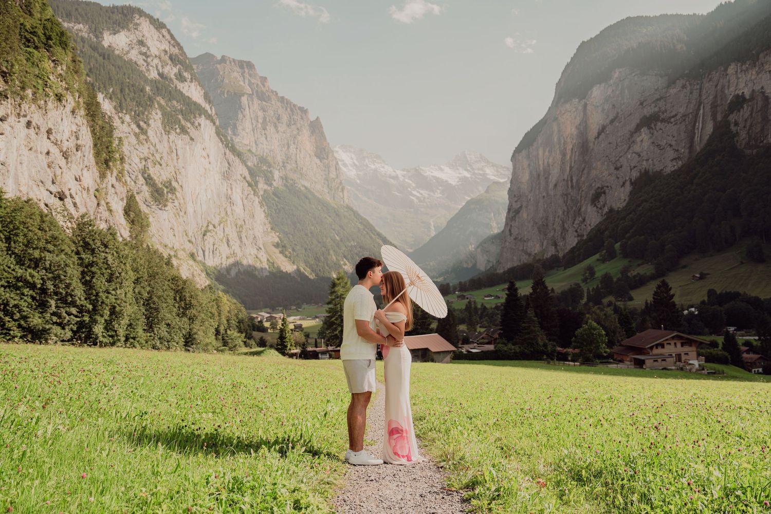 Couple embracing and kissing on a scenic meadow path with the stunning Lauterbrunnen valley and Alps behind them.