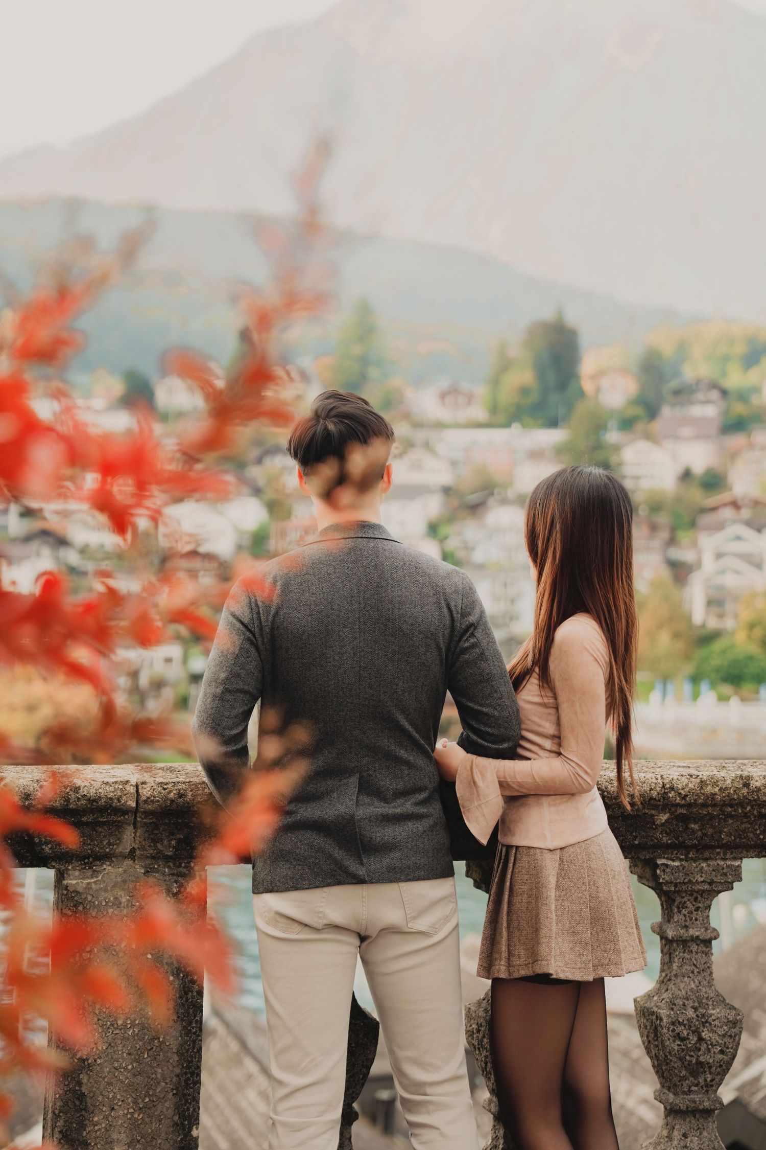 Couple embracing on a stone balcony overlooking a misty Swiss alpine village.