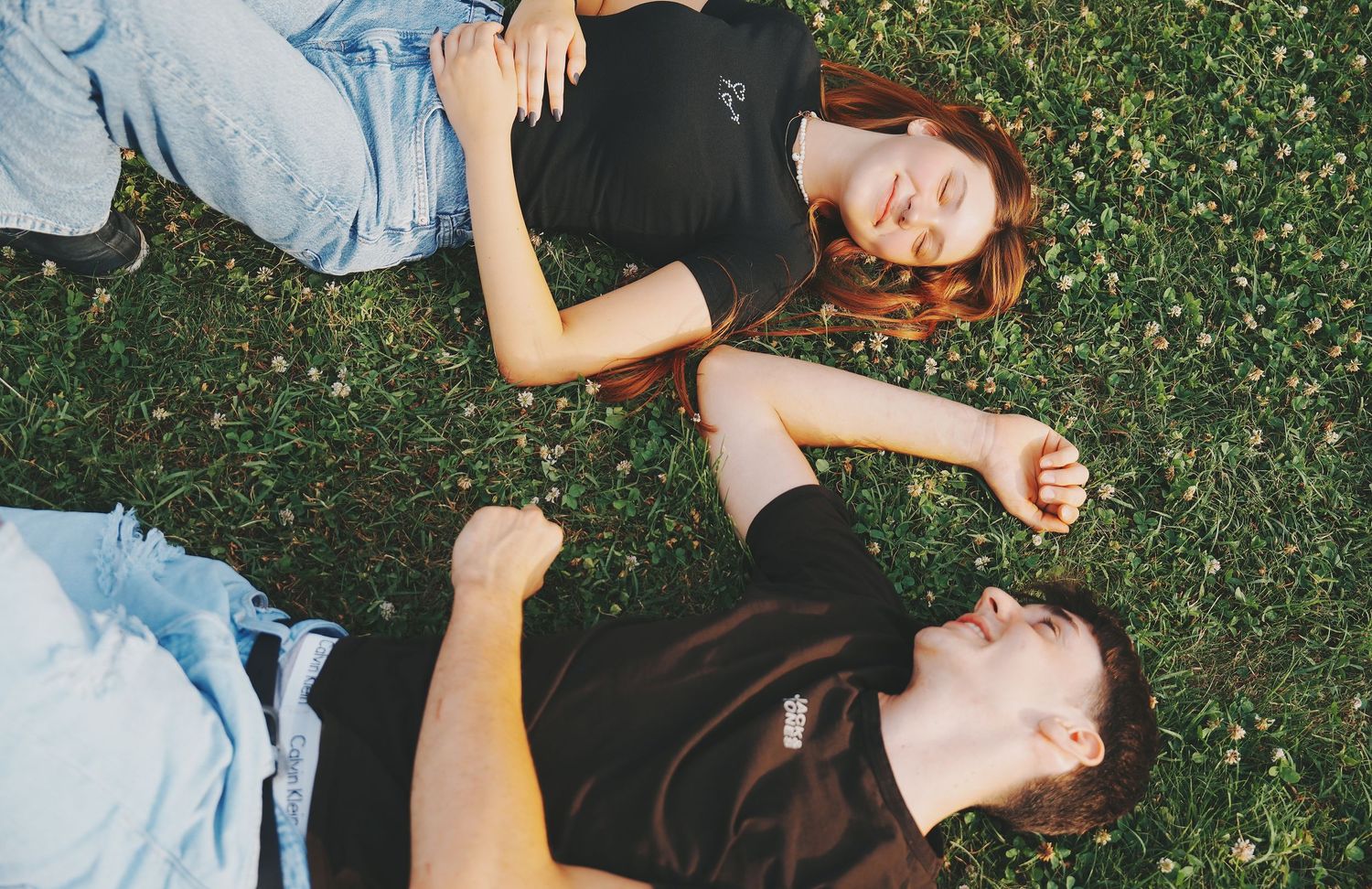 Couple lying on grass together laughing with eyes closed on a sunny day.
