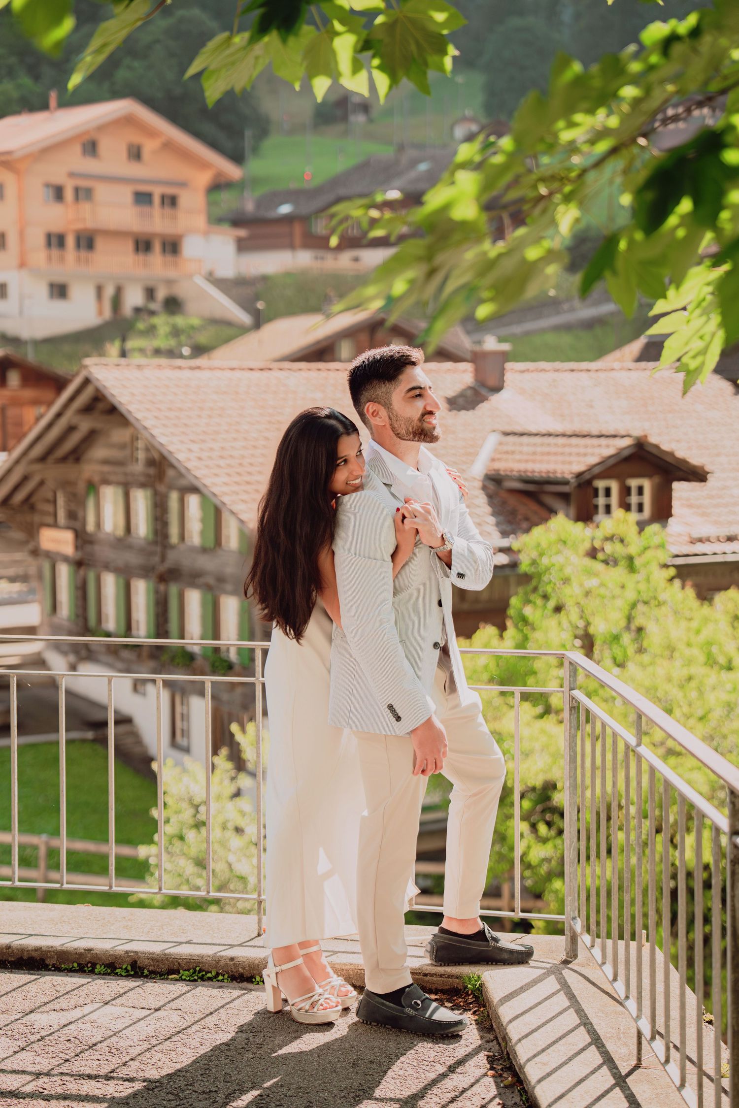 Couple embracing on a terrace overlooking traditional Swiss chalet-style buildings.