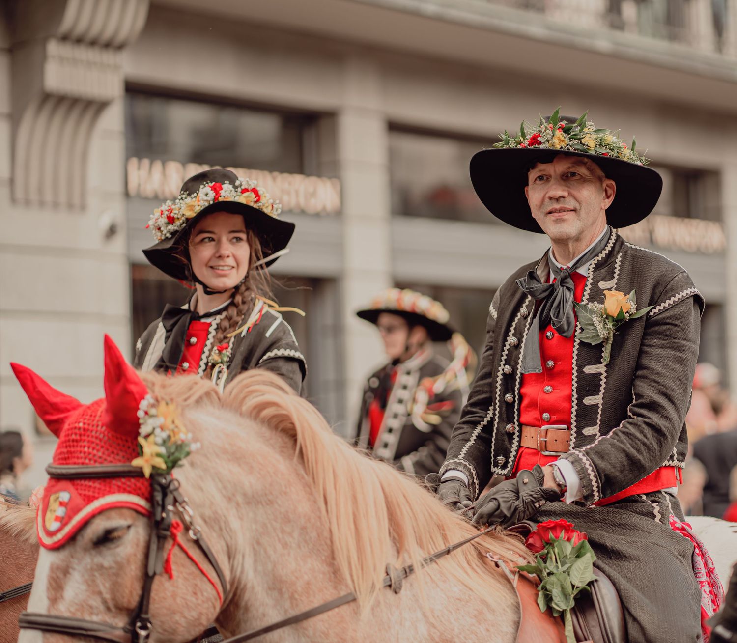 Two riders in traditional Swiss costumes on decorated horses during a cultural parade.