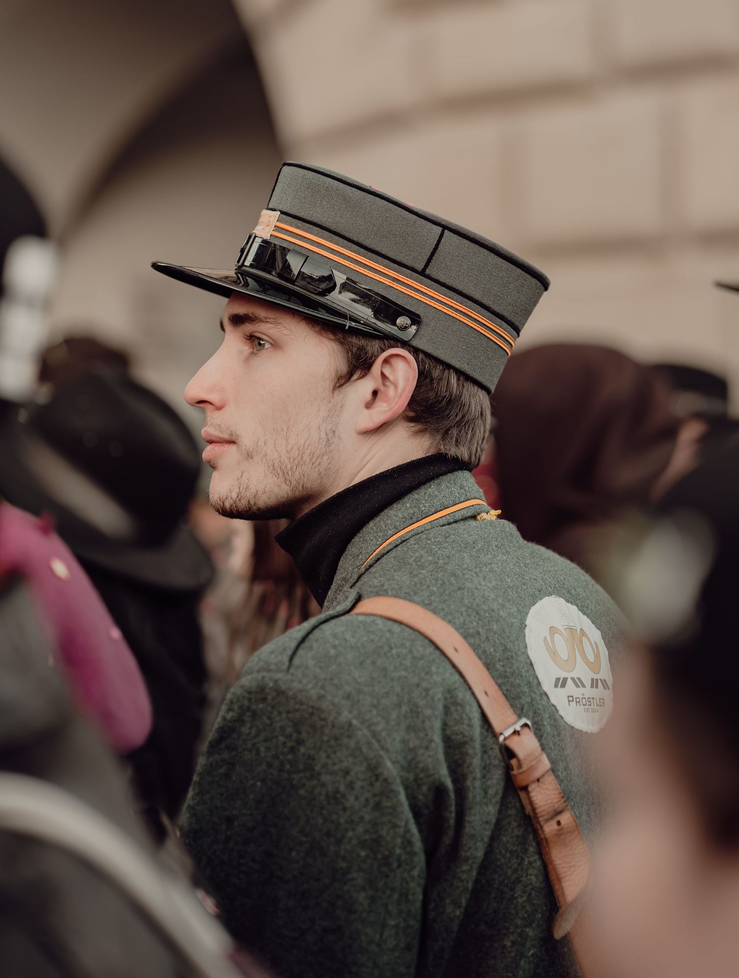 Young man in vintage military uniform with gray cap at crowded festival.
