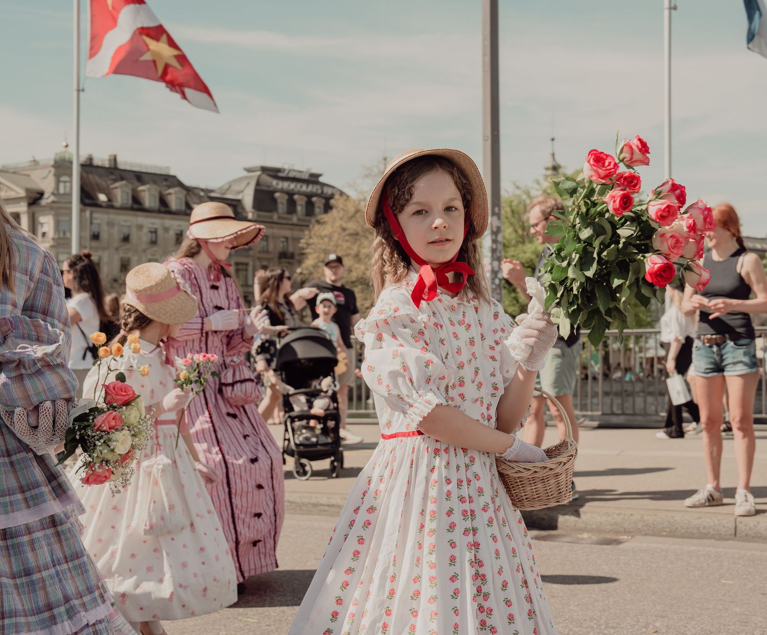 Young girl in white floral dress holding red roses walks in a traditional Swiss cultural street parade.