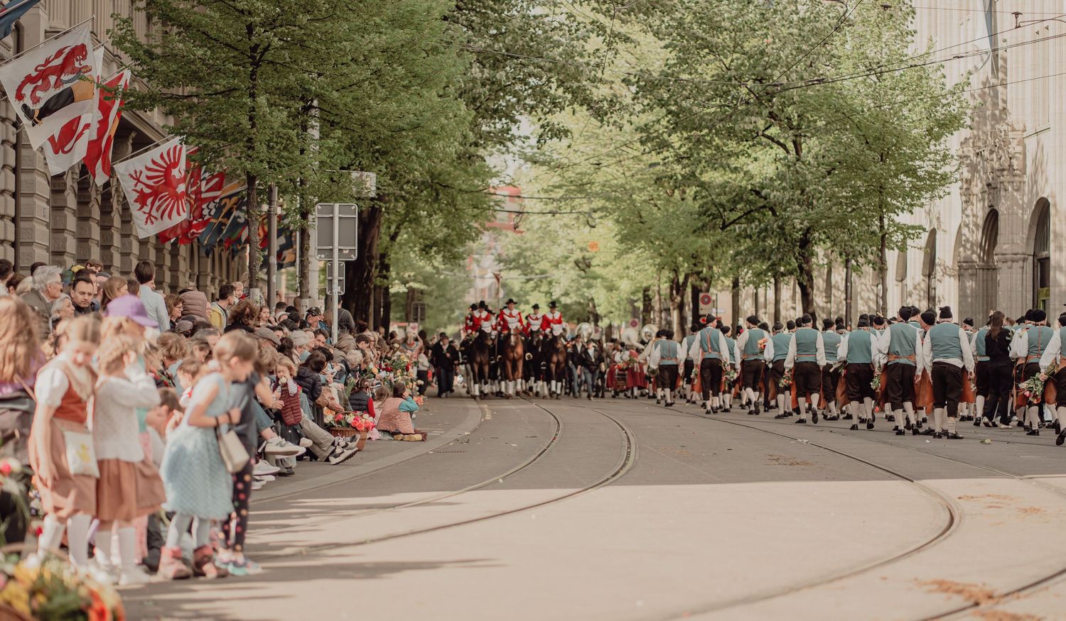 Large group of children in blue uniforms march in a street parade lined with spectators.