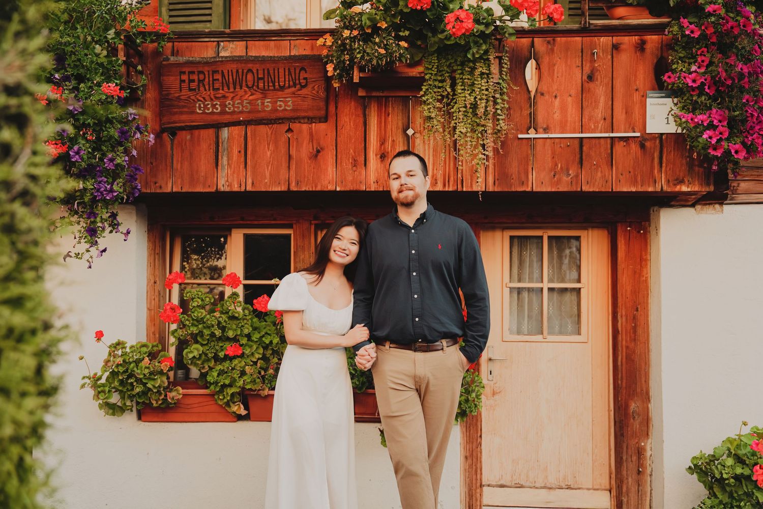 Couple posing together outside a traditional Swiss Ferienwohnung with lush floral decorations.