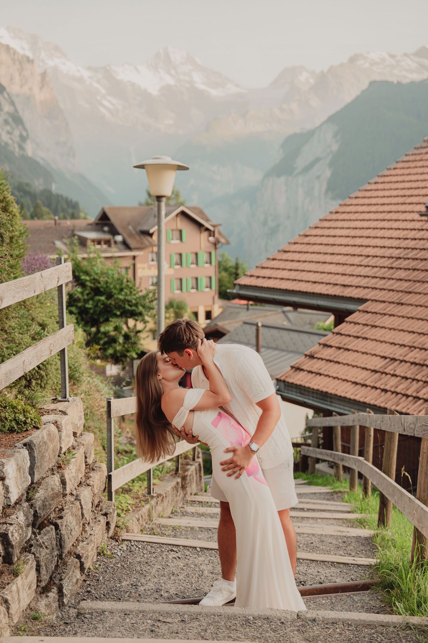 Romantic couple sharing a dip kiss on scenic stairs in Swiss mountain village Lauterbrunnen.