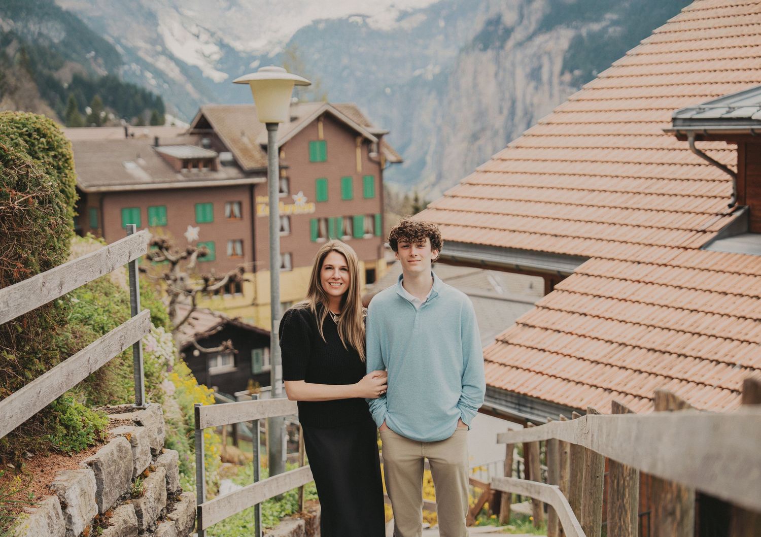 Mother and teenage son smiling together on steps in a charming Swiss mountain village.