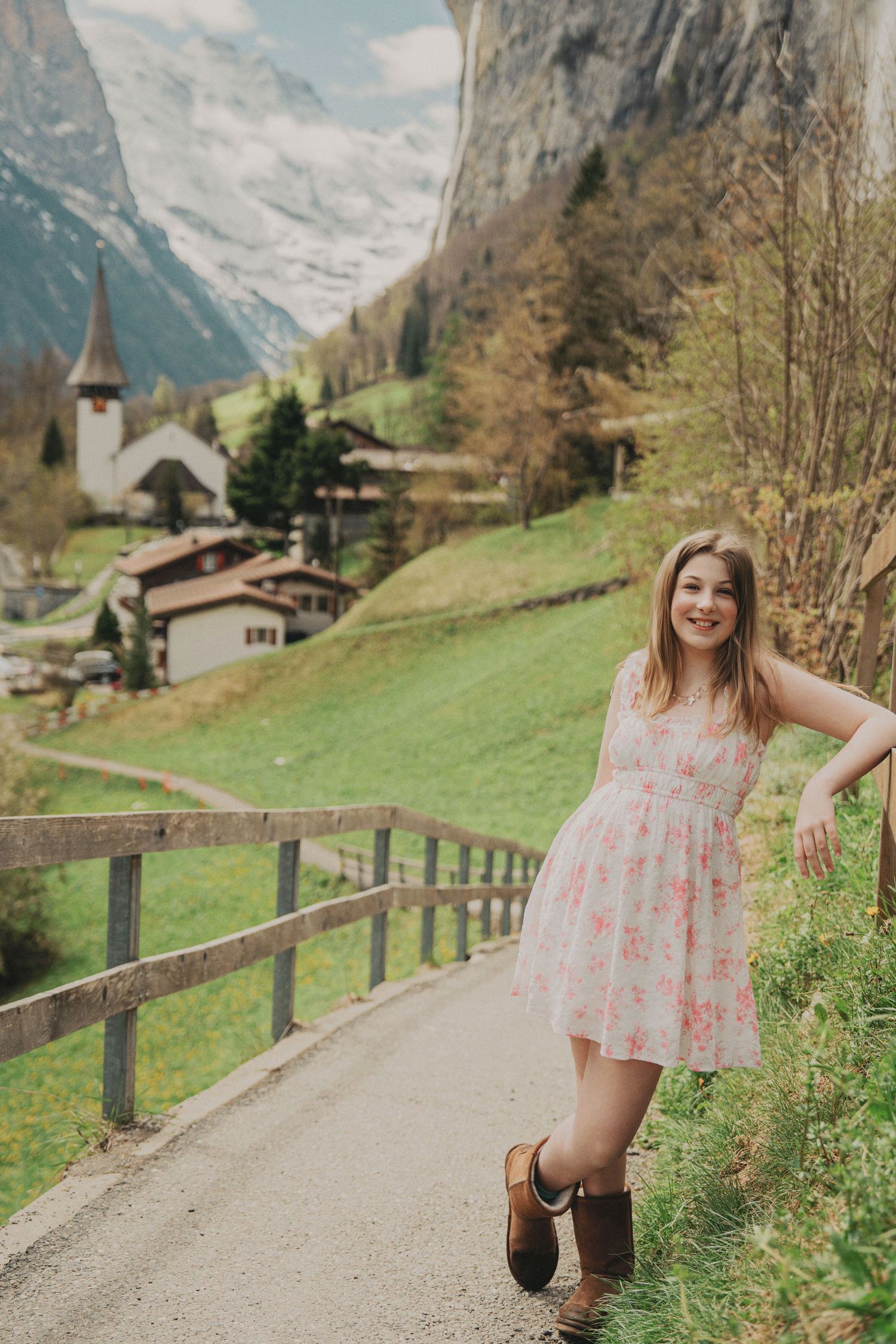 Smiling young girl in a pink floral dress standing on a path in a beautiful Swiss mountain village.
