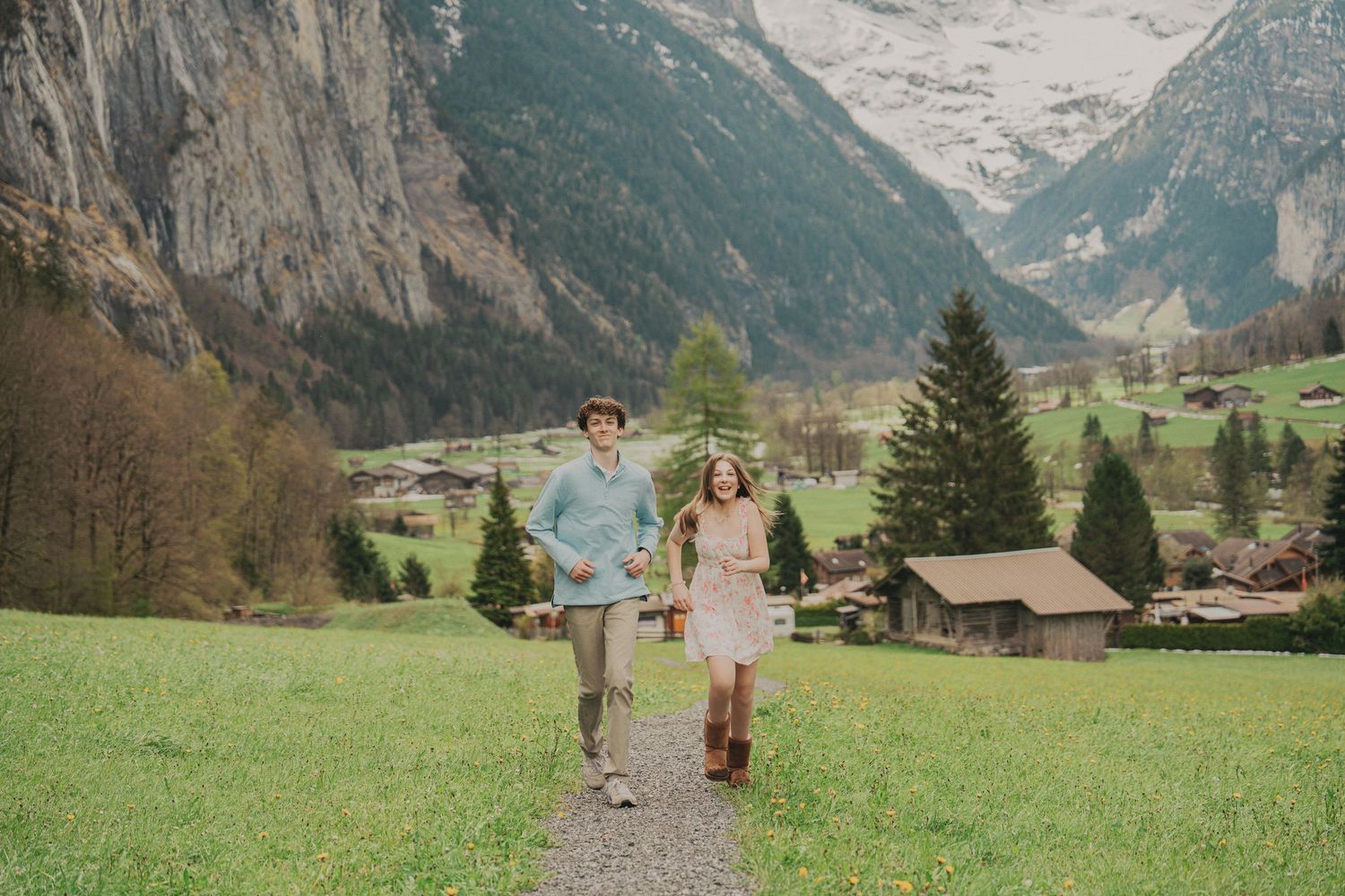 Happy couple running together on a scenic mountain path in a picturesque Swiss Alpine valley with snow-capped peaks.