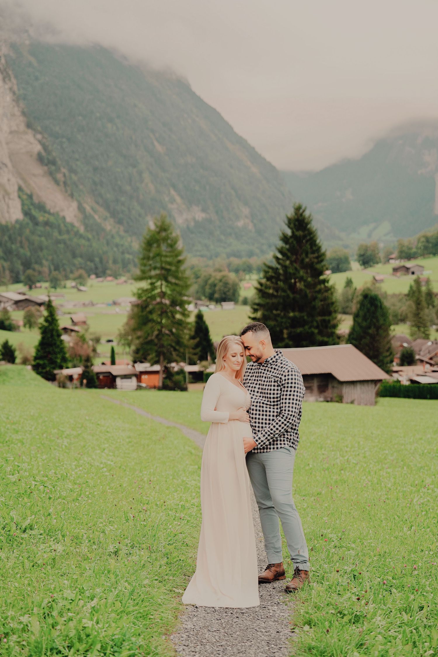 Man embracing pregnant partner on scenic path in Lauterbrunnen Switzerland with green valley and mountains.