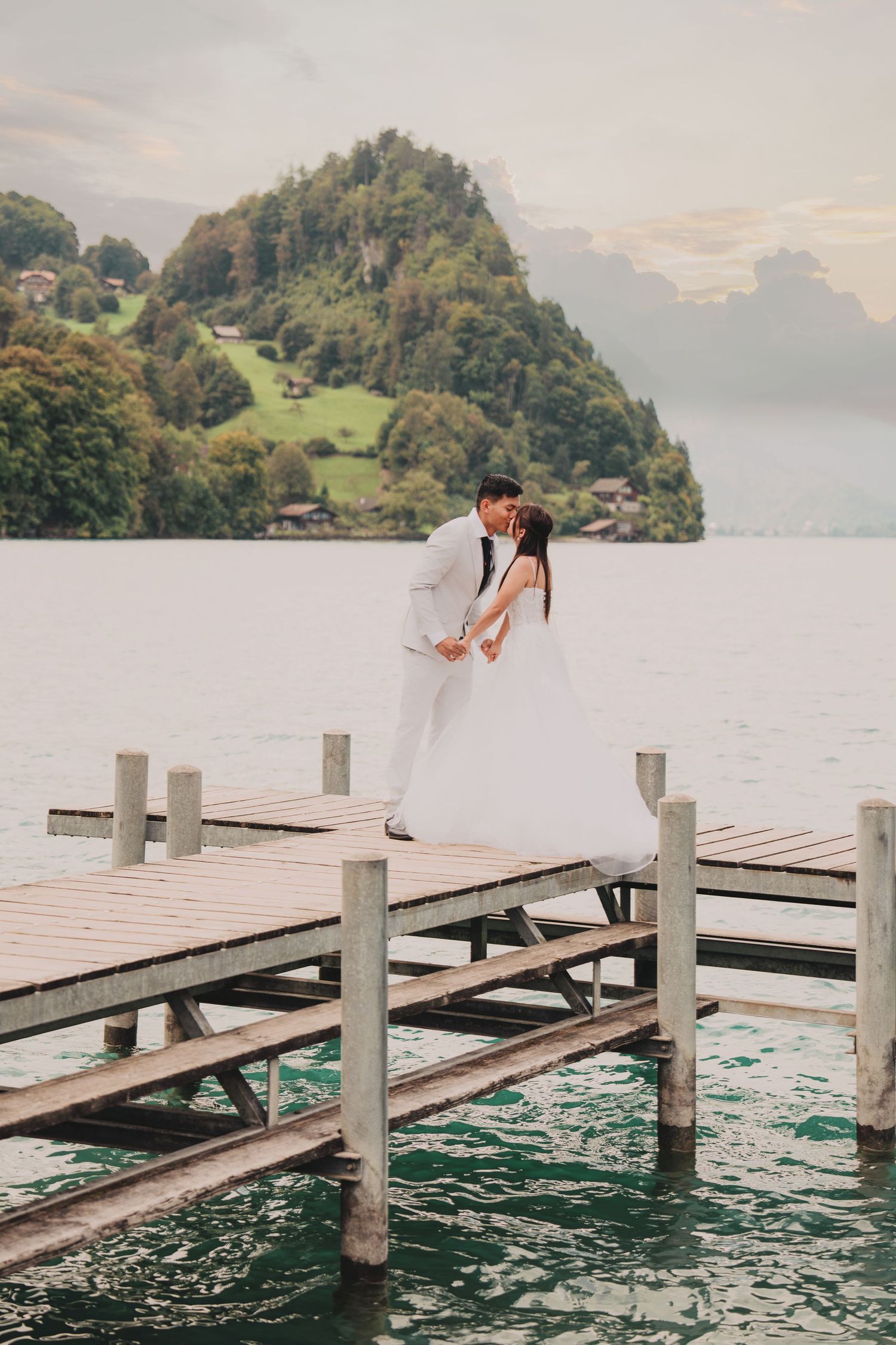 Bride and groom sharing a romantic kiss on a wooden pier over a stunning alpine lake.