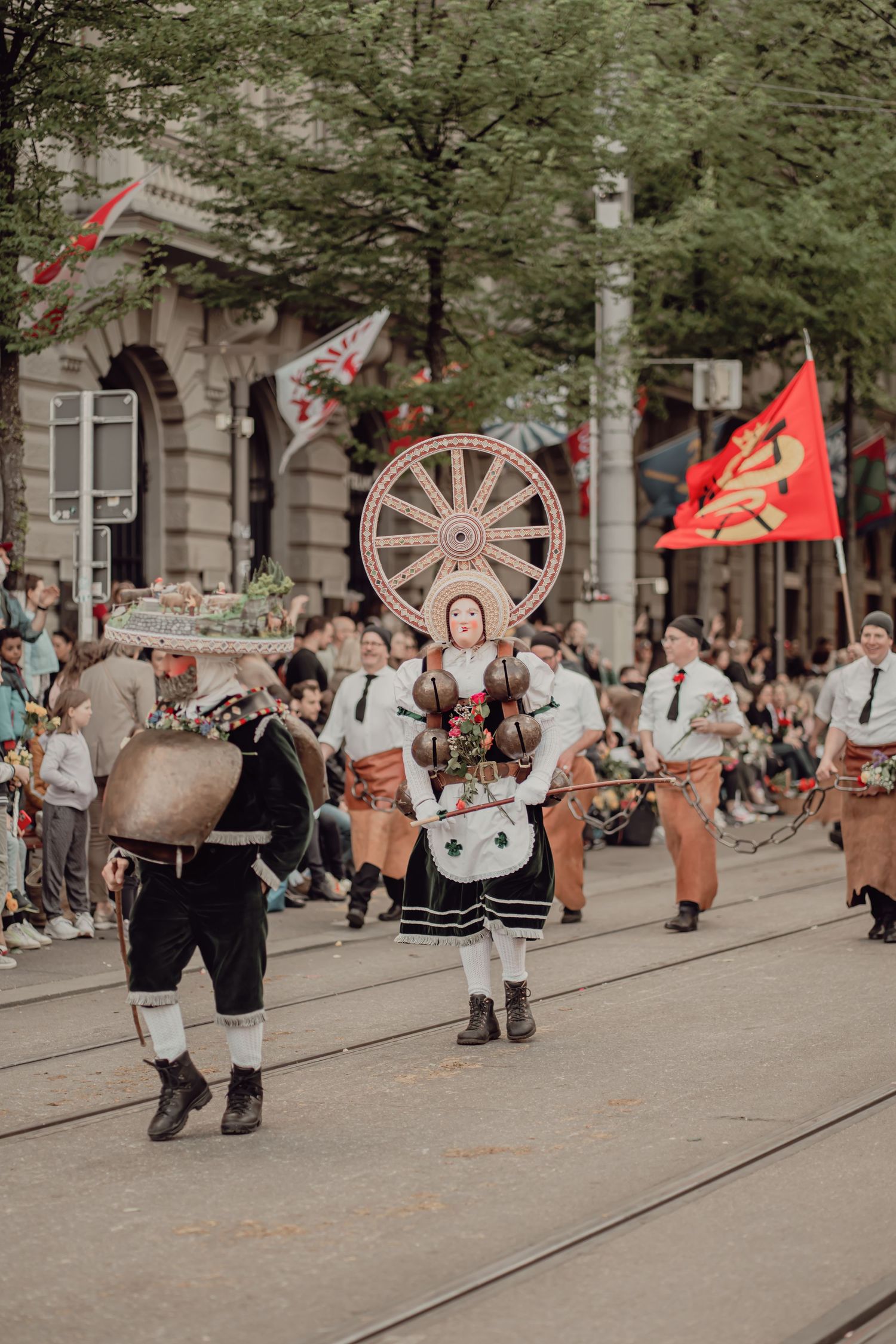 Folk parade performers in traditional costumes carrying decorative wheel and bells.
