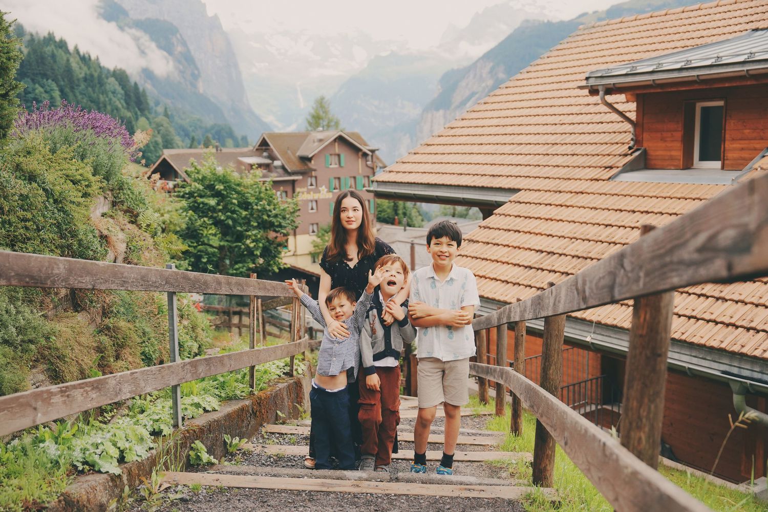Woman with three young boys posing on wooden bridge steps in a charming Alpine mountain village.