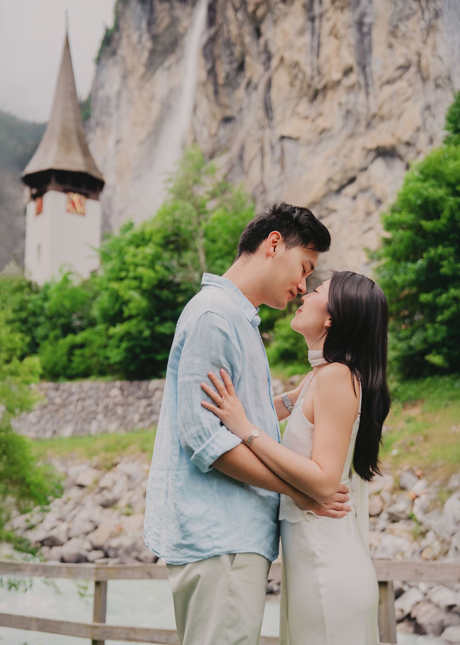 Couple sharing a romantic kiss near Staubbach Falls and a historic church in Lauterbrunnen, Switzerland.