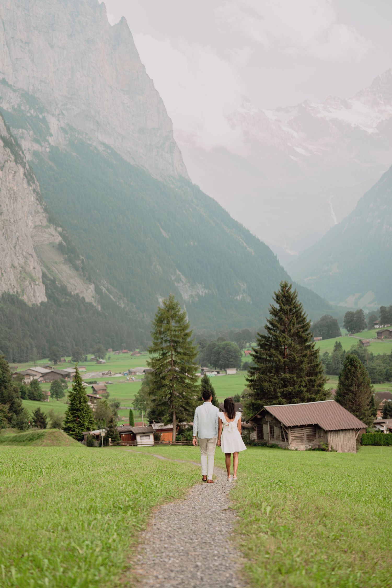 Couple walking hand in hand on a path through a lush Alpine valley with dramatic mountain peaks in Switzerland.