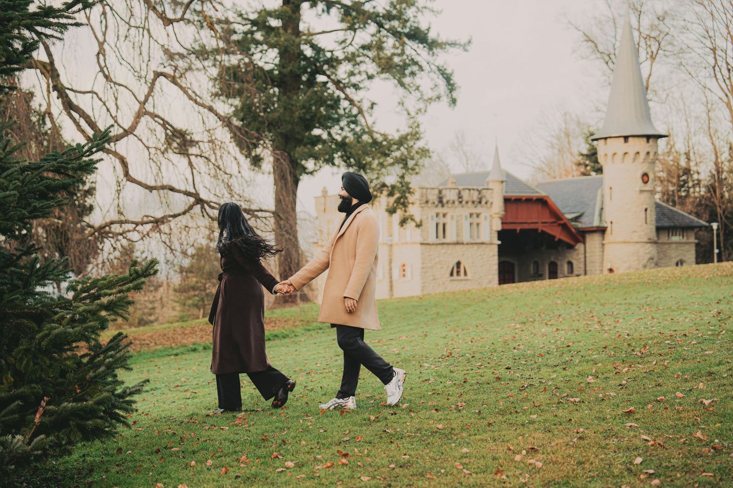 Couple walking hand in hand toward castle through autumn park.