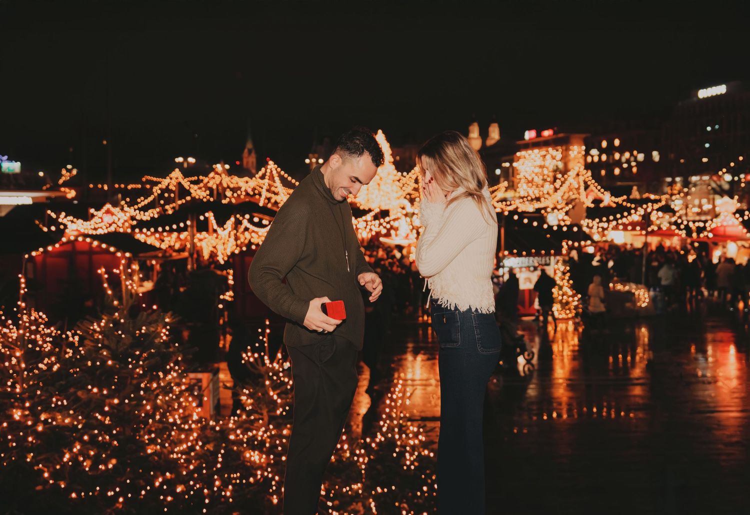 Couple sharing a romantic moment at a festive Christmas market glowing with warm golden lights at night.